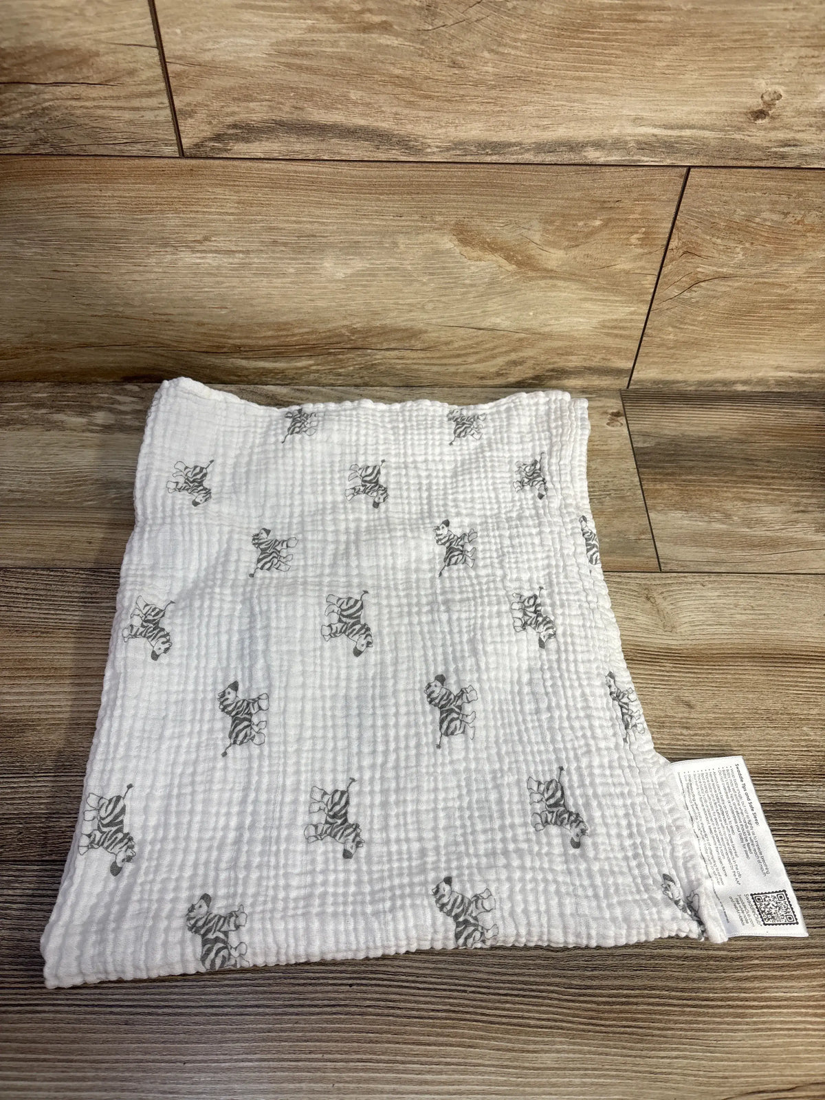 Overhead view of Amazing Baby muslin swaddle blanket showcasing white muslin fabric with gray zebra print on a wood floor