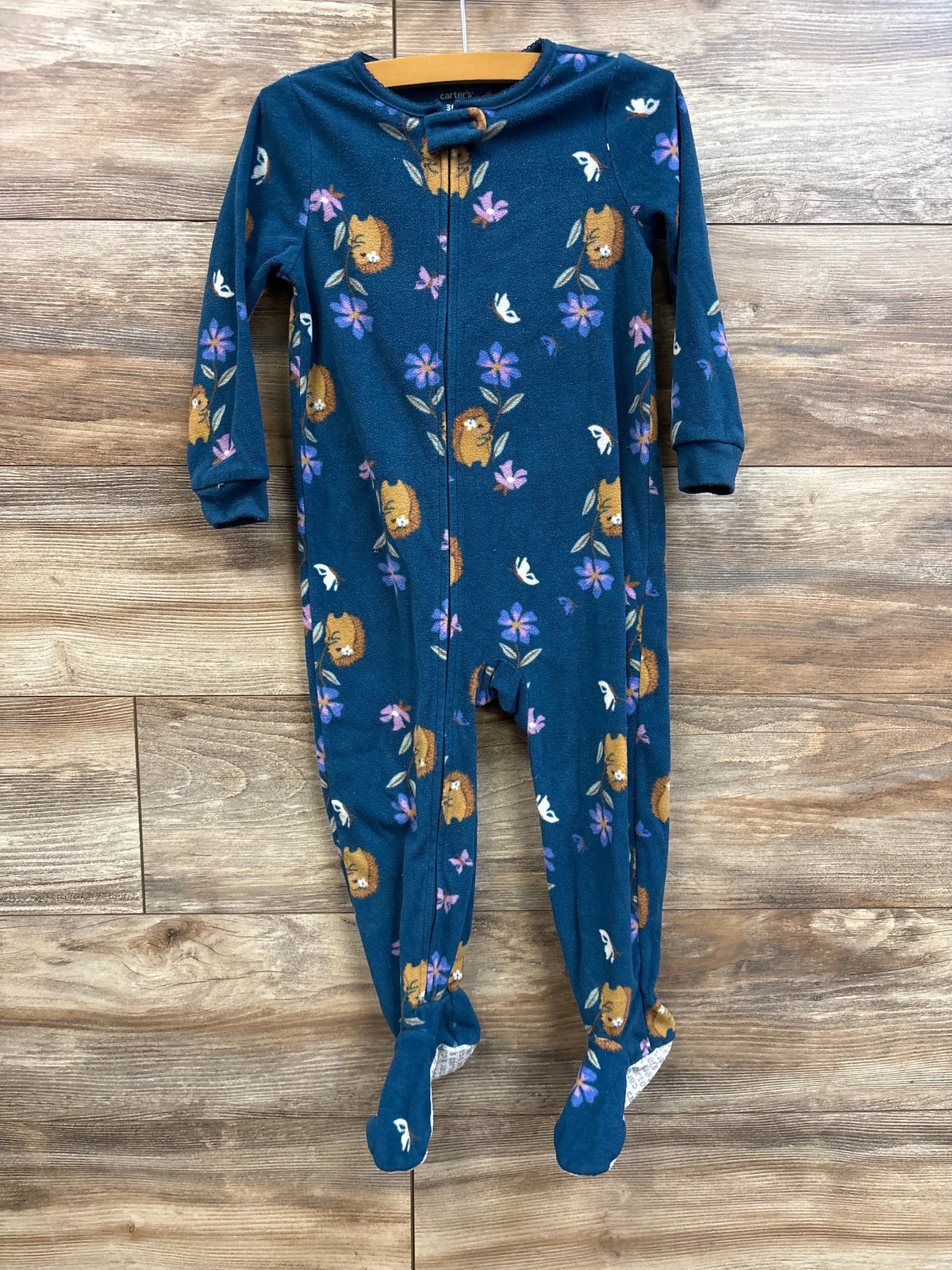 Front view of Carter’s blue footed blanket sleeper, size 3T, showcasing zipper front and lion-and-flower print with wooden plank background