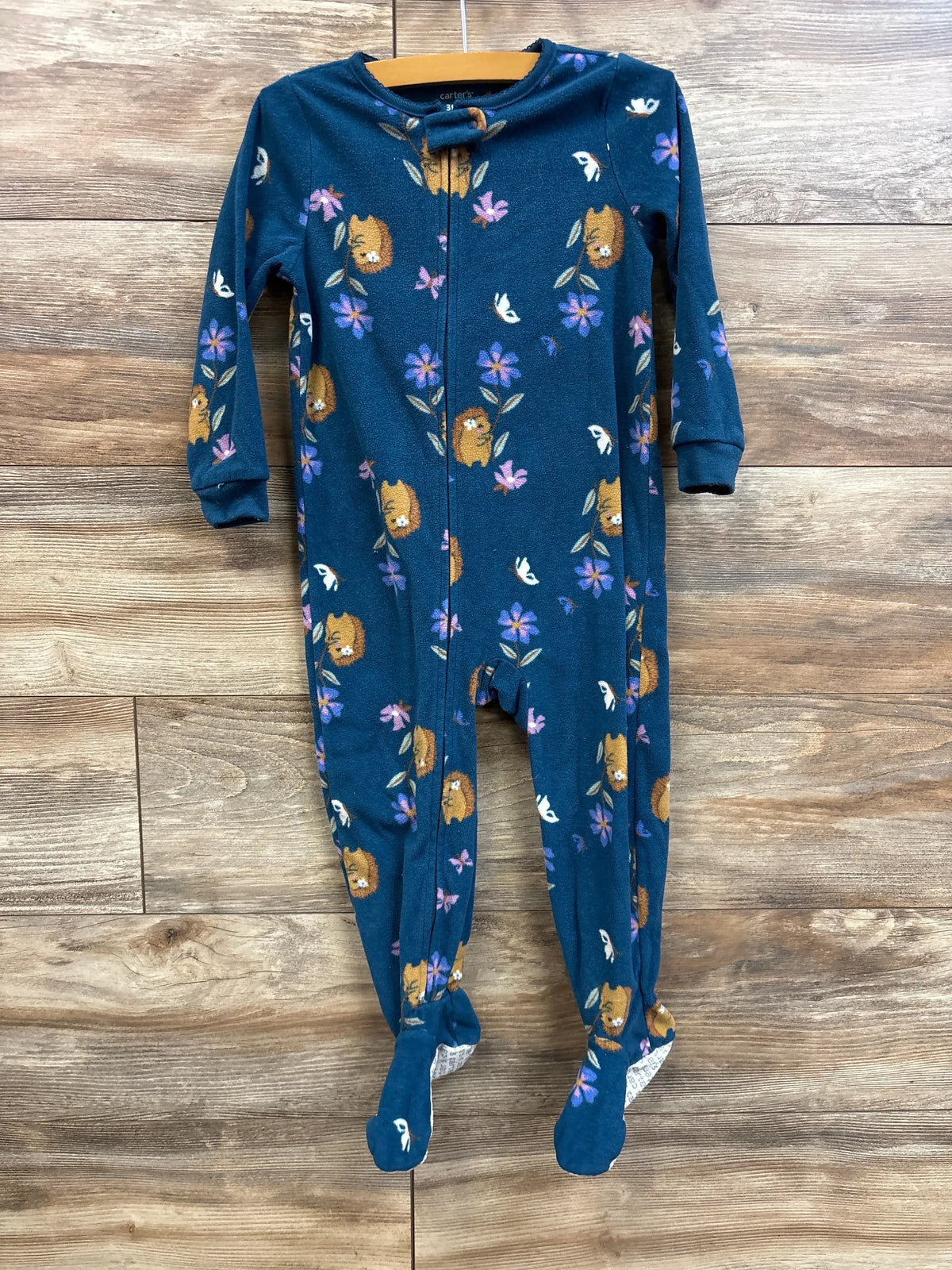 Front view of Carter’s blue footed blanket sleeper, size 3T, showcasing zipper front and lion-and-flower print with wooden plank background