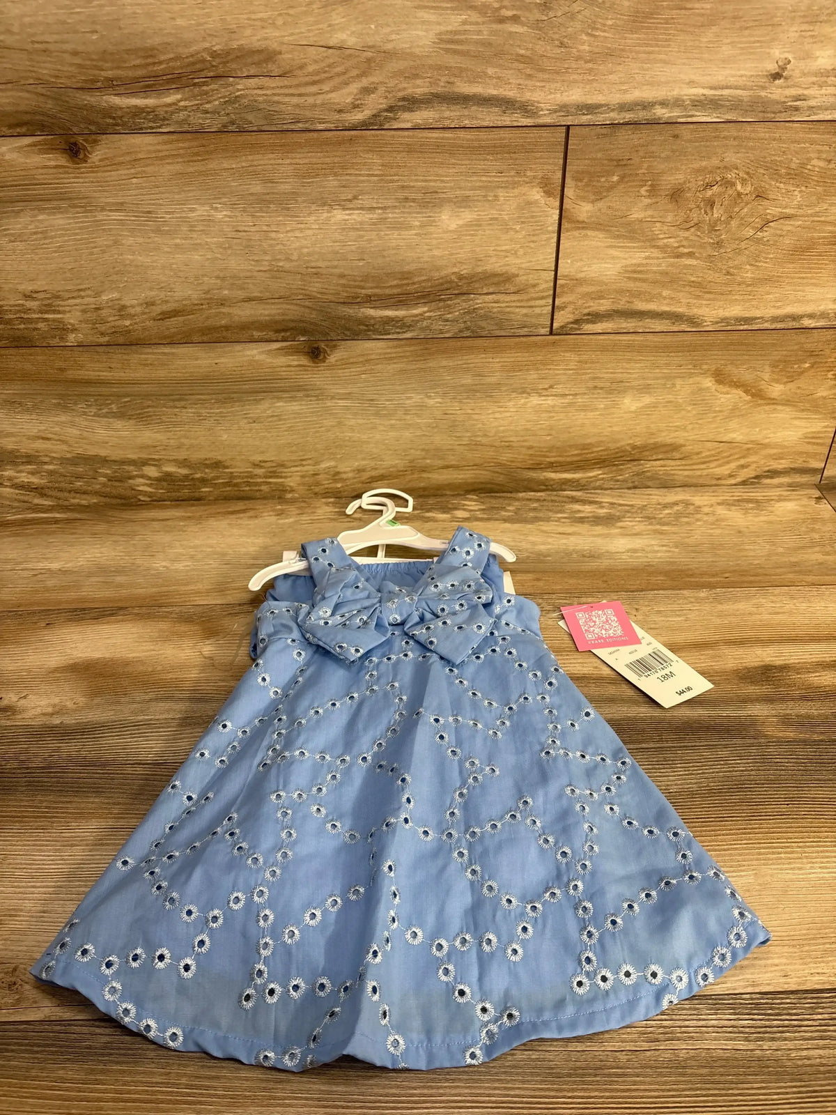 Front view of blue eyelet dress and bloomers set with embroidered floral cutouts and bow detail on wood background size 18M