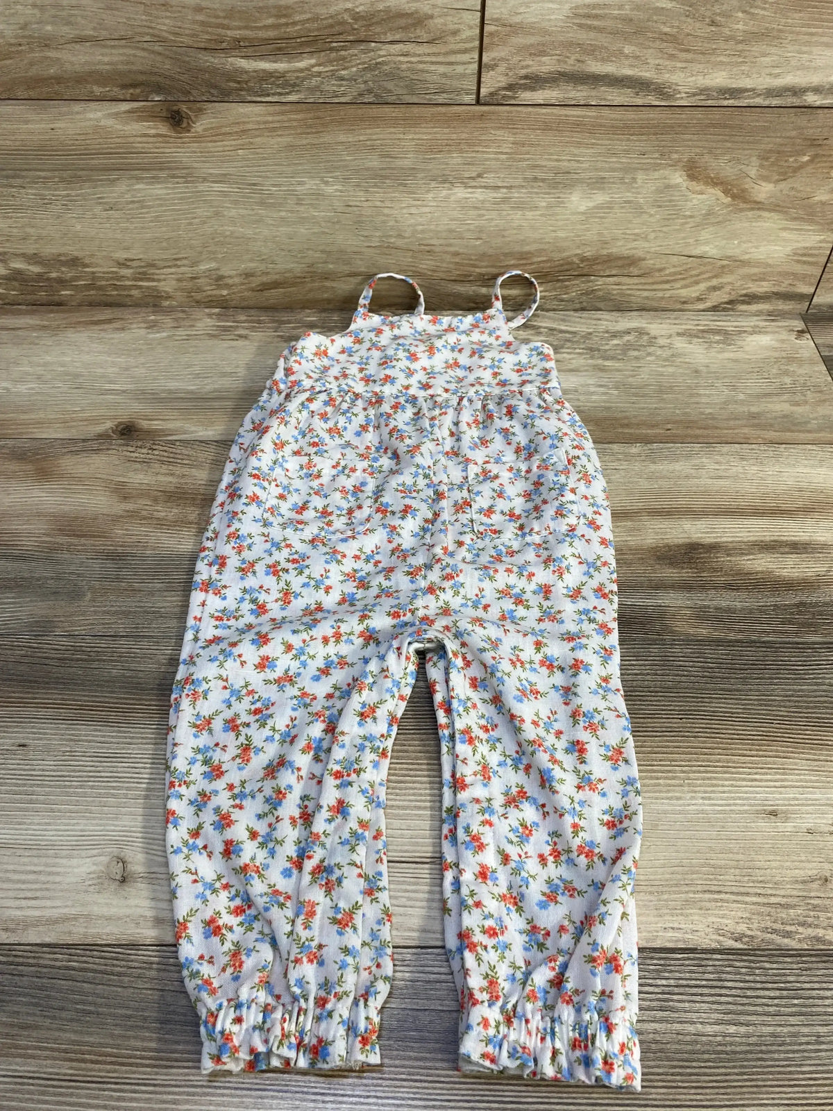 Front flat-lay of white Old Navy sleeveless floral jumpsuit with front pockets and elastic ankle cuffs on wood floor background