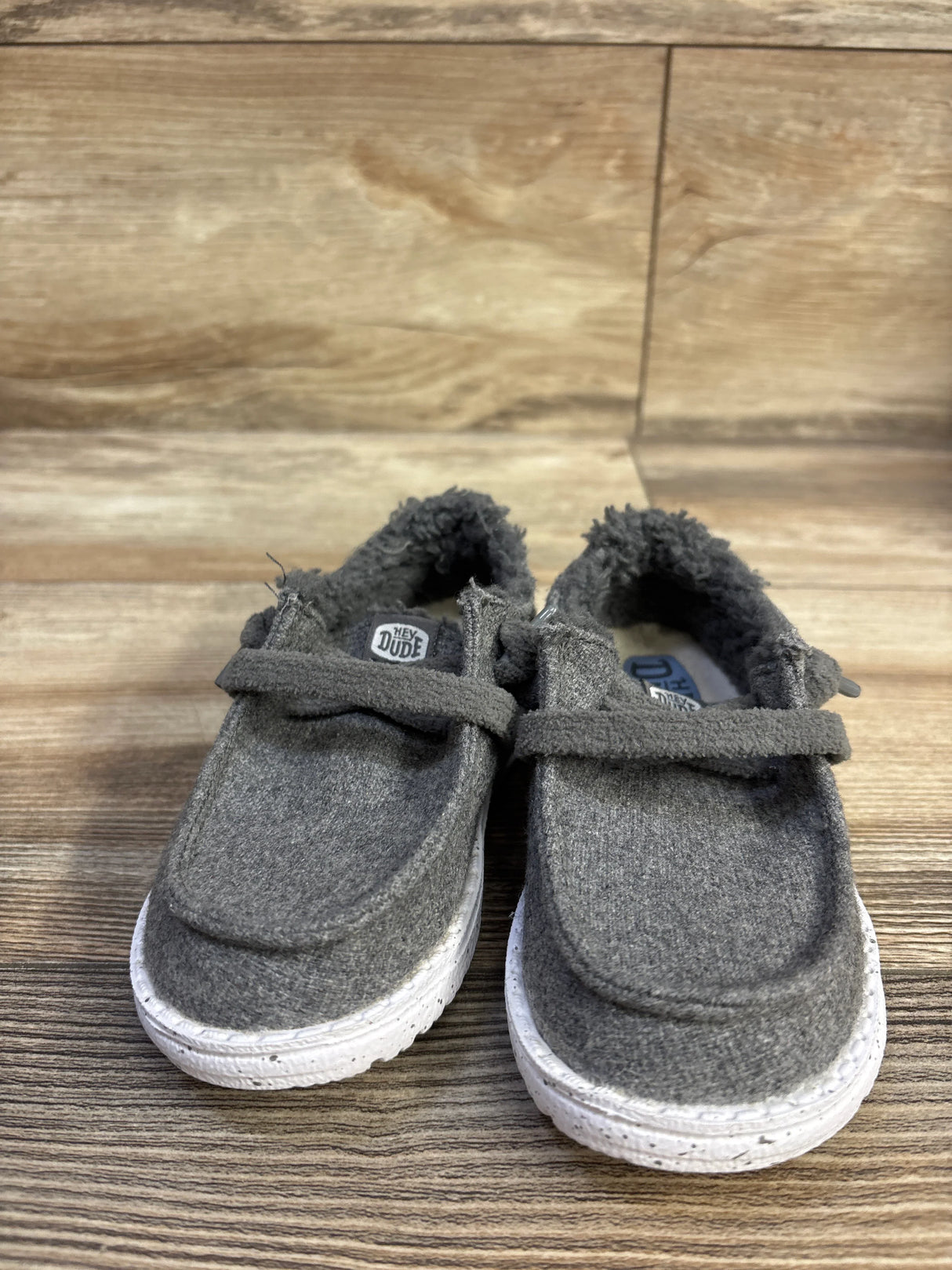 Front view of Hey Dude Wendy Wool kids slip-on shoes showing grey wool upper, fuzzy lining and white speckled sole on wood floor