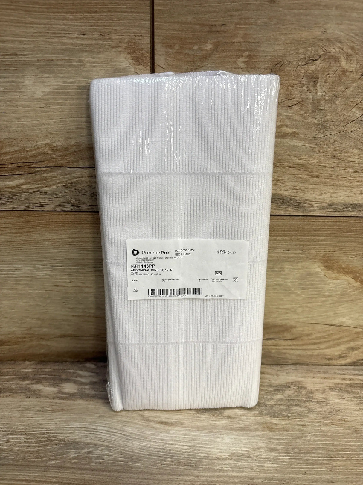 Front view of Premier Pro abdominal binder folded, white ribbed elastic with label stating 12 in width and size 46-62 in on wood background