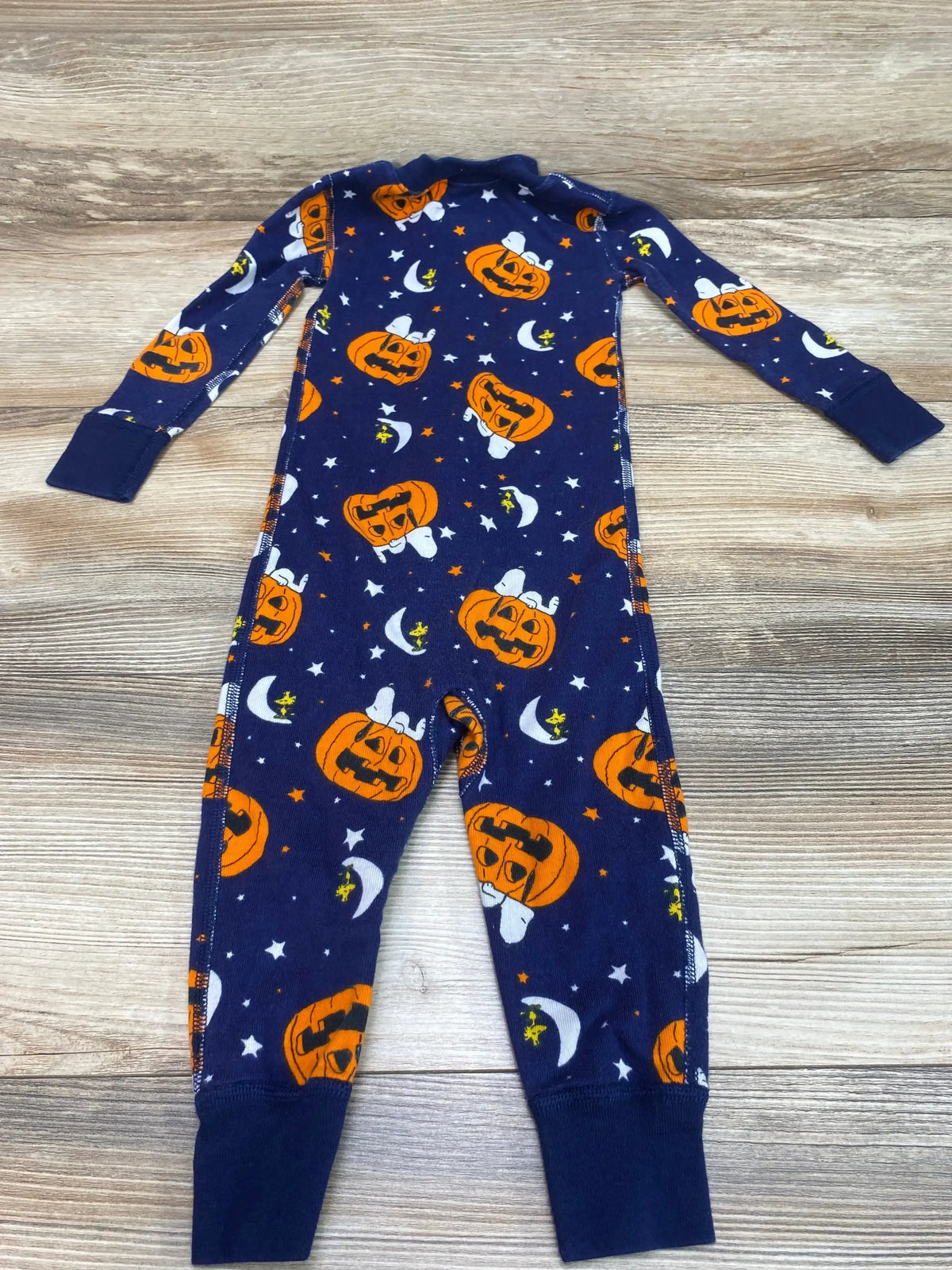 Flat lay of Hanna Andersson Peanuts Halloween zip sleeper, navy with orange pumpkin faces and Snoopy print, zip front and cuffed feet on wood