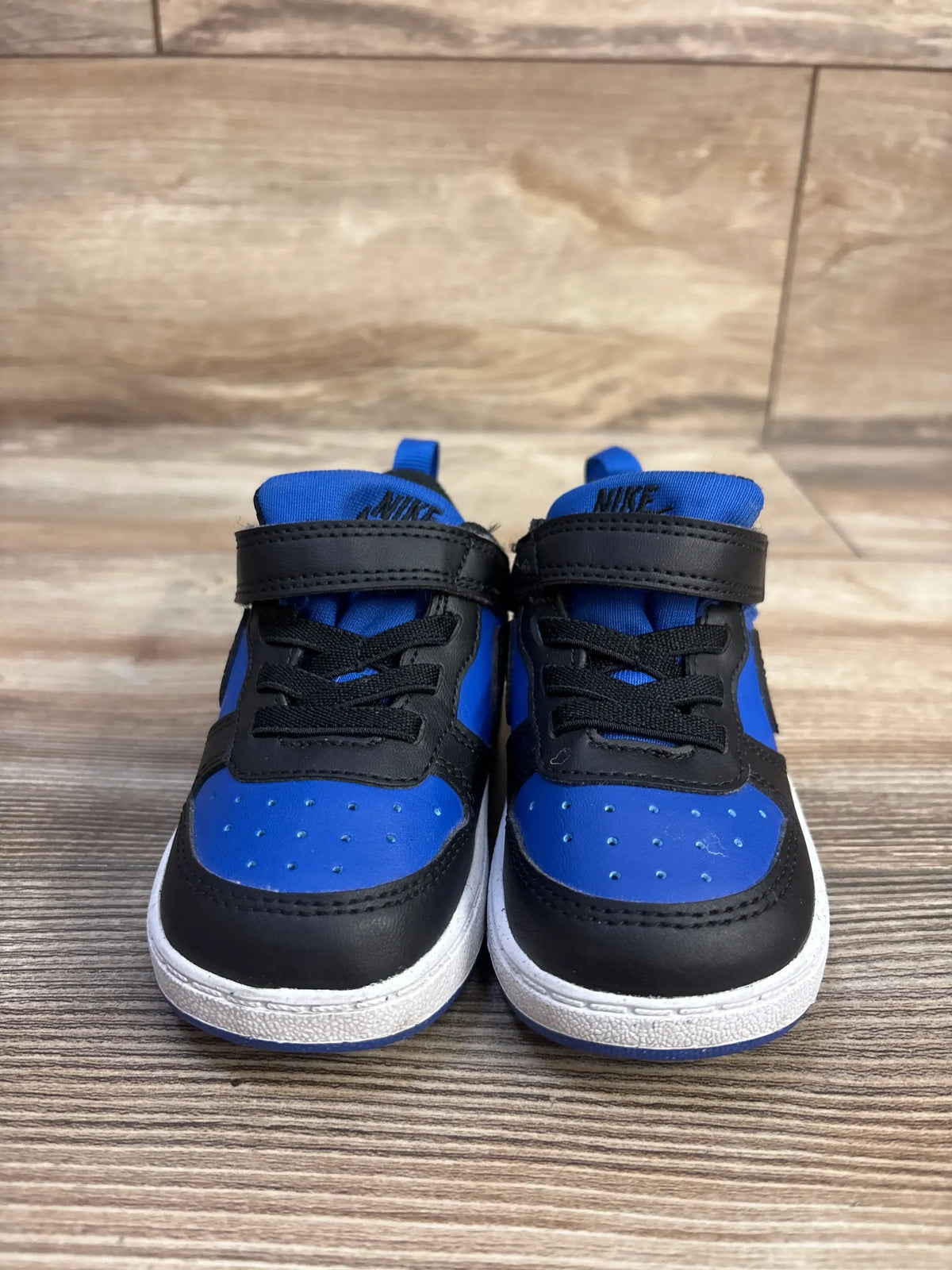 Front view of Nike Court Borough Recraft TD sneakers in Game Royal and Black with hook and loop straps on wood flooring