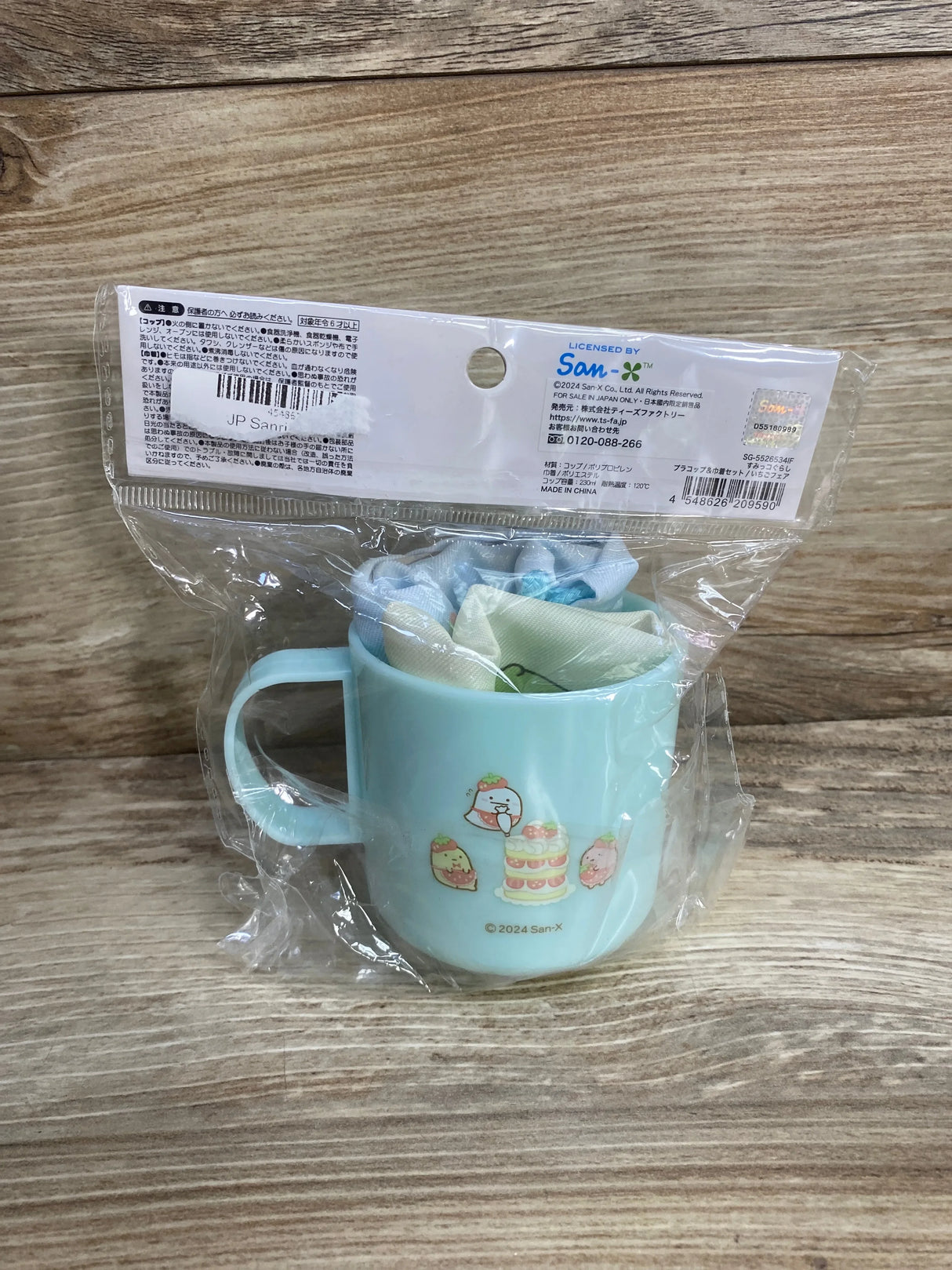 Front view of NEW Sumikkogurashi Cup and Drawstring Bag Set showcasing mint green plastic cup with character print in sealed San-X packaging on wood plank floor