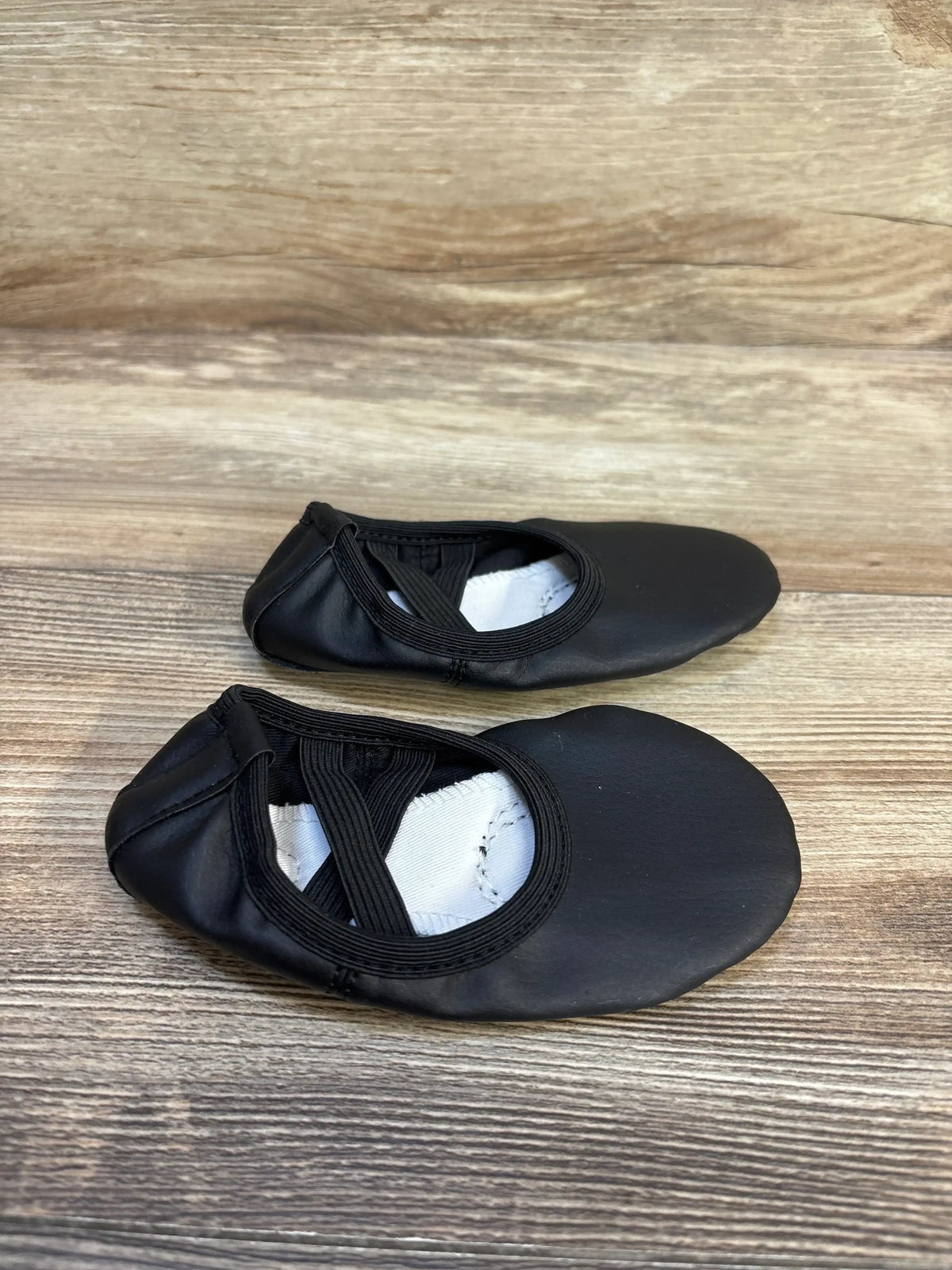 Pair of black children's ballet slippers with elastic straps on wooden surface