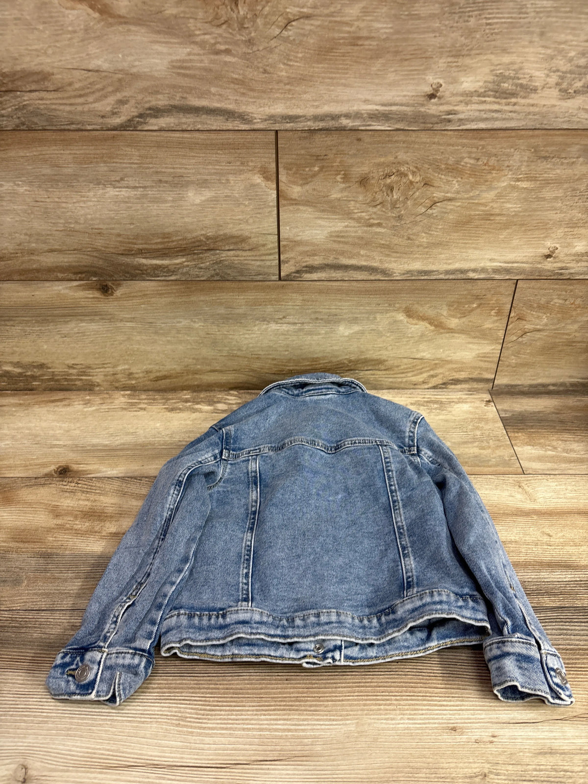 Back view of a blue Jumping Beans denim jacket for kids size 5T on a wood background