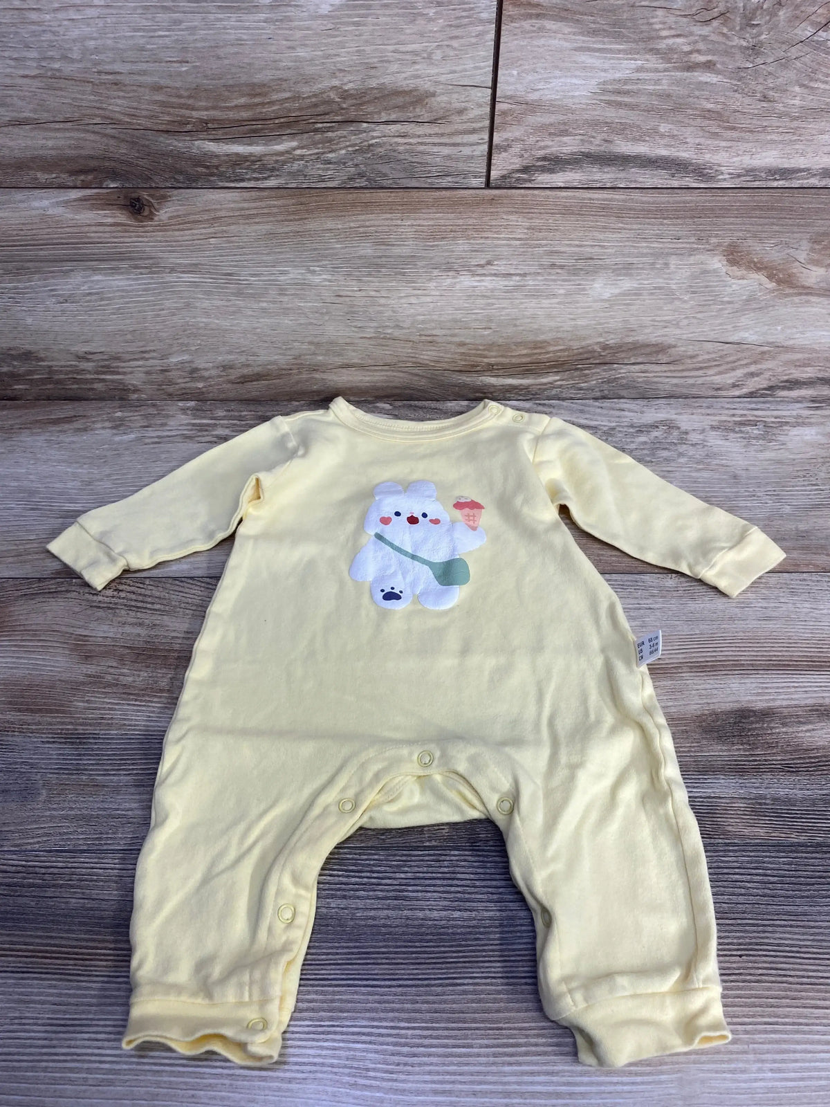 Front view of yellow baby coverall showing bunny patch with ice cream, shoulder and crotch snap closures, laid flat on wood background