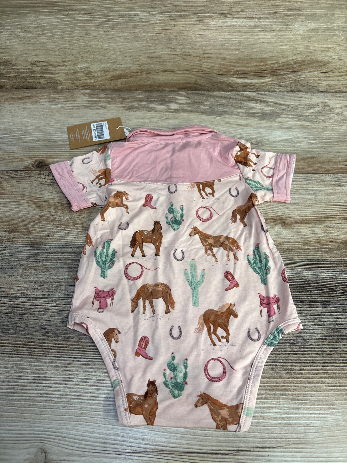 Pink baby onesie with horse, cactus, cowboy hat and boot pattern on wood background