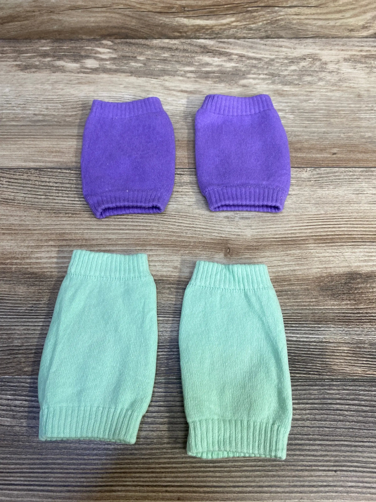 Top-down view of baby crawling knee pads in purple and mint showcasing knit fabric and elastic cuffs on wood