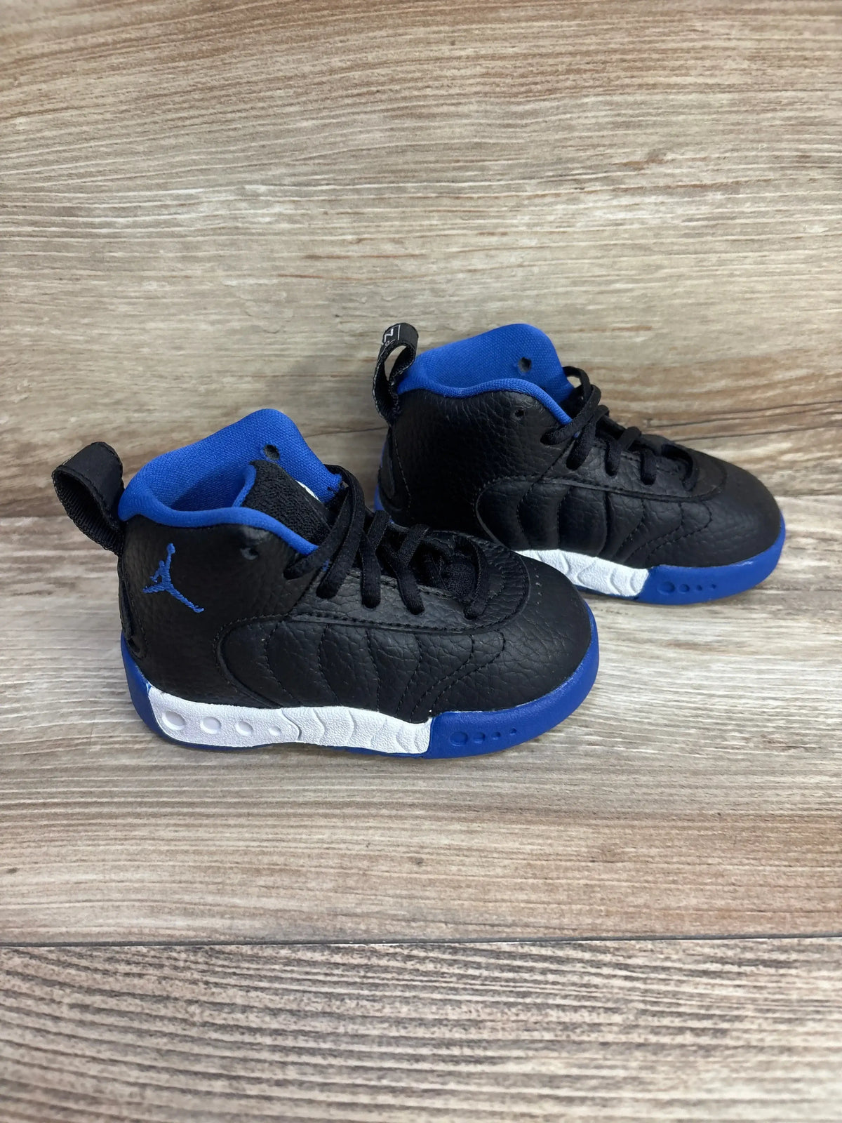 Three-quarter view of toddler Air Jordan Jumpman Pro BT sneakers with black pebbled upper, blue lining and outsole, white midsole accents on wood background