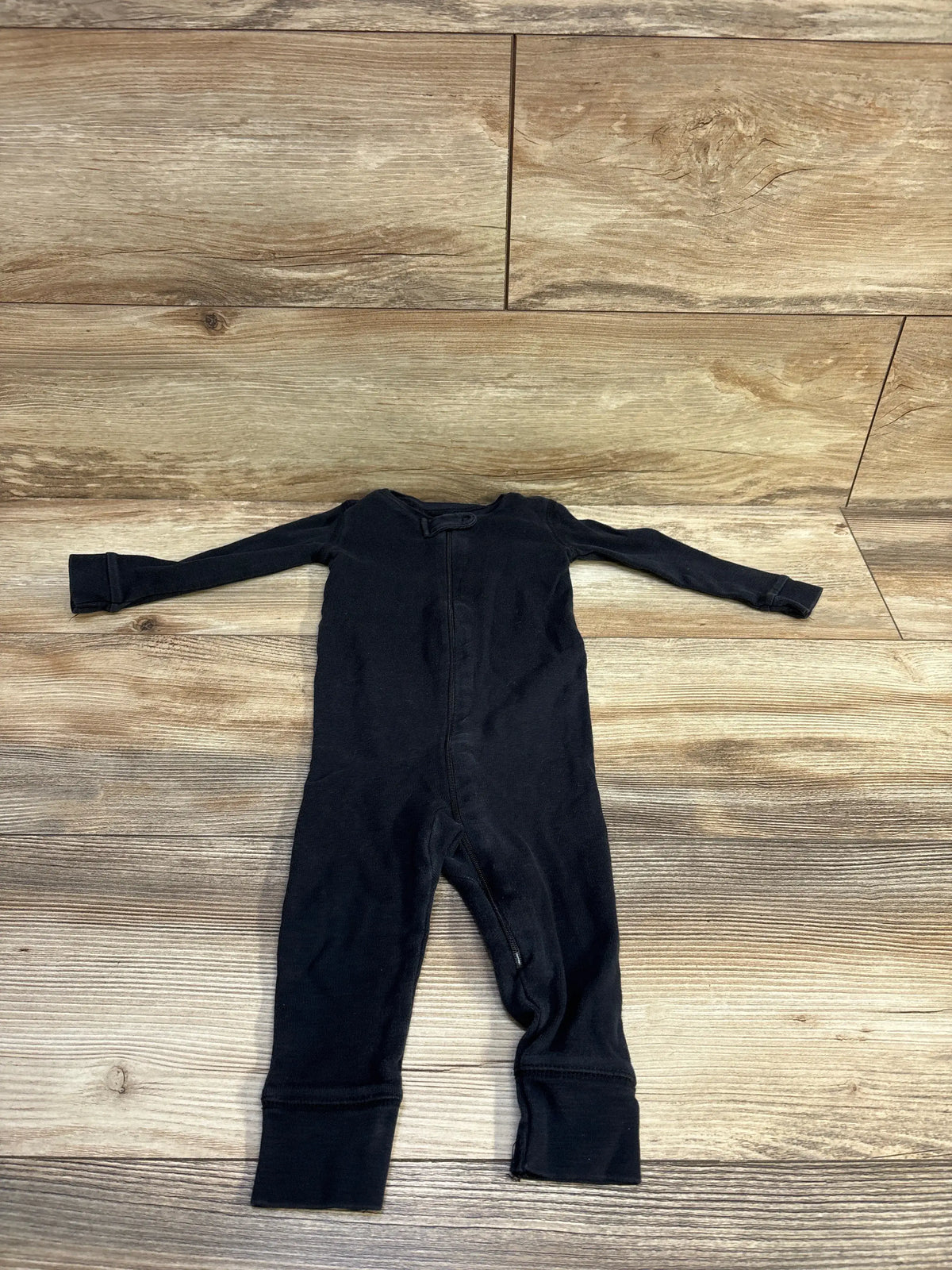 Flat lay of Primary organic sleeper in black, size 9–12 months showcasing front zipper and fold-over cuffs on wood floor background