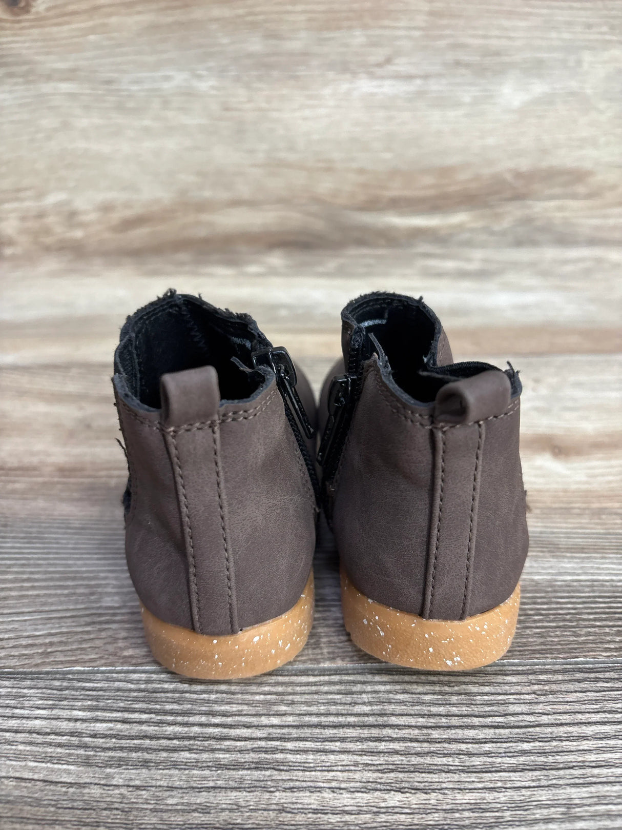 Pair of small brown toddler boots with tan speckled soles on wood floor