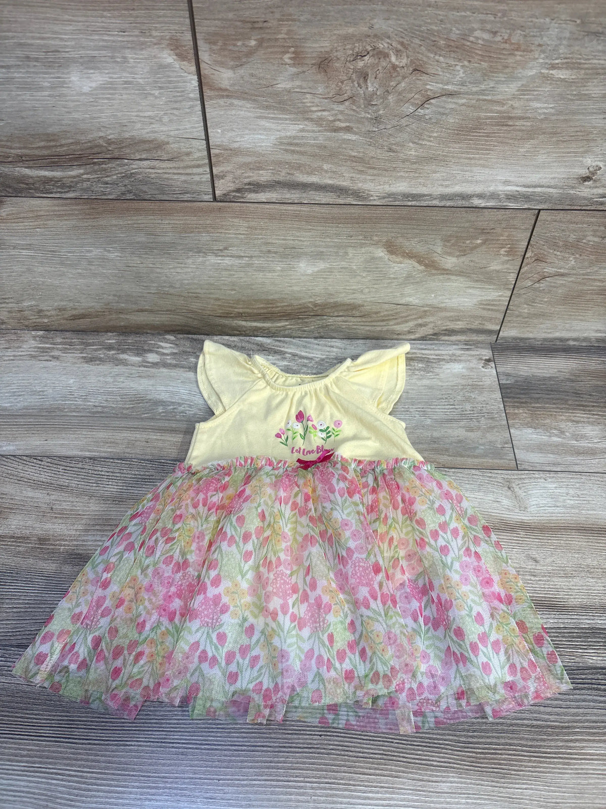 Front view of Kids Headquarters yellow floral tulle overlay dress with cap sleeves and Let Love Bloom text on wood flooring