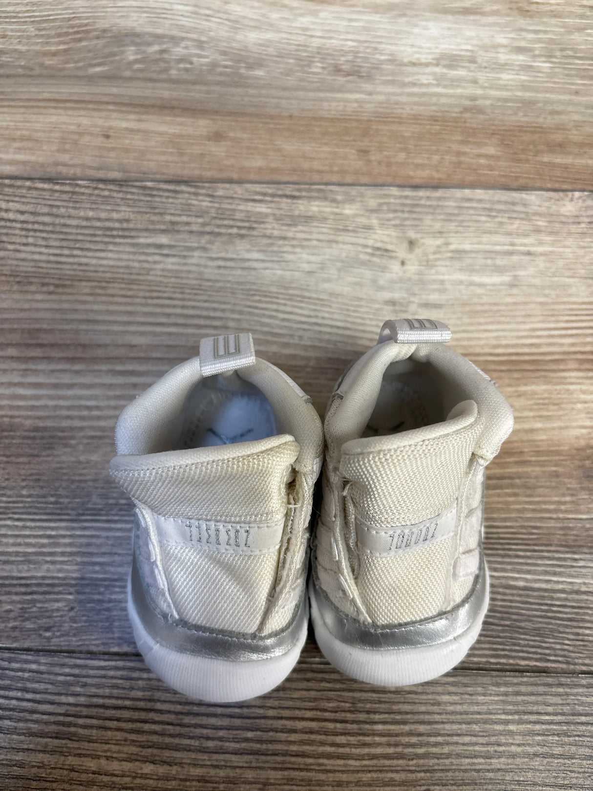 Cream and silver baby sneakers on wooden floor, gently used kids footwear