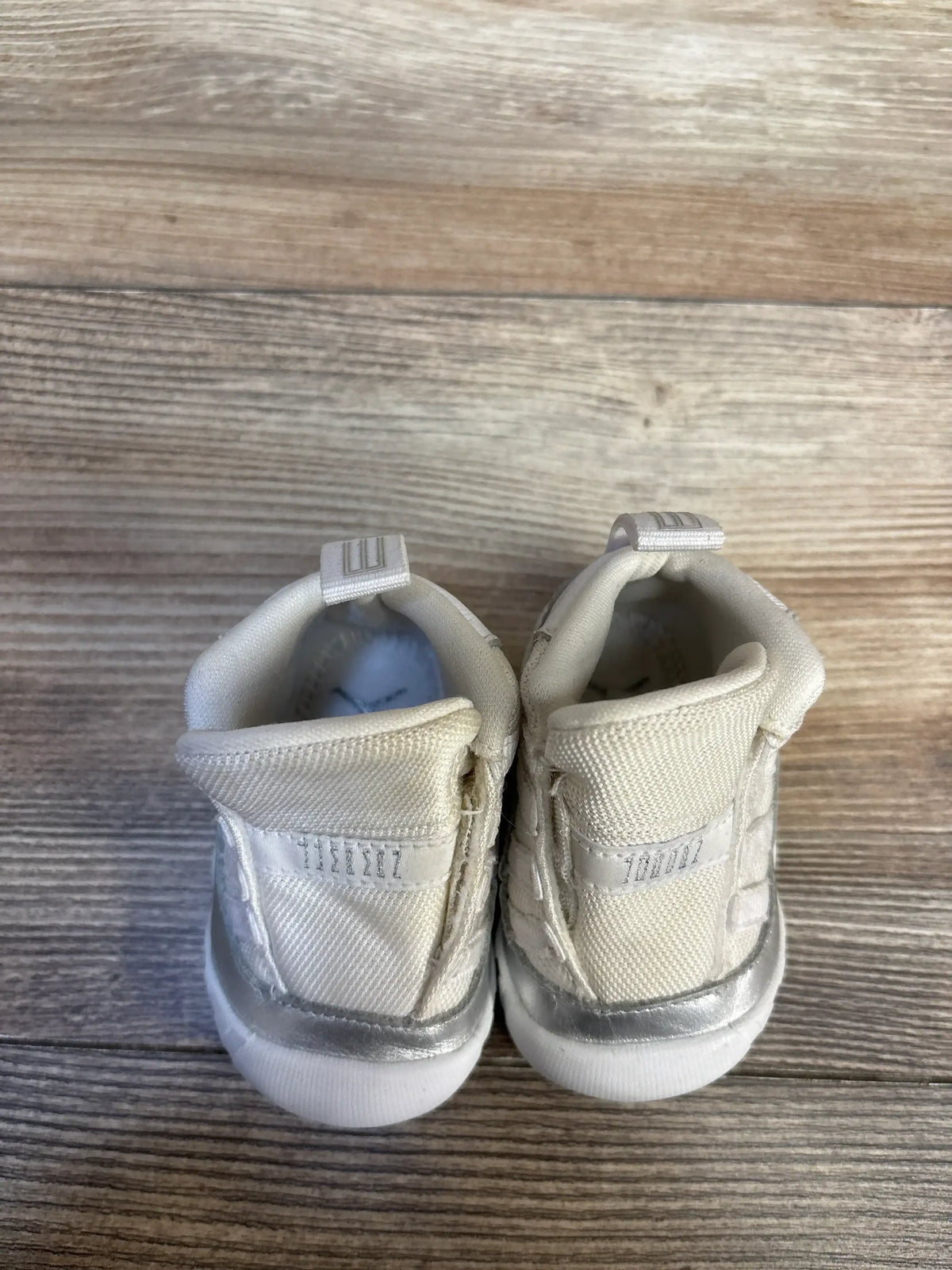 Rear view of Air Jordan 11 Retro TD Metallic Silver sneakers size 2C showing cream upper and silver heel on wood floor