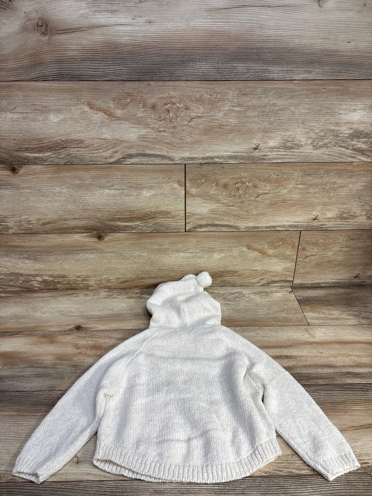 White knit hooded sweater with pom-pom on wooden floor background