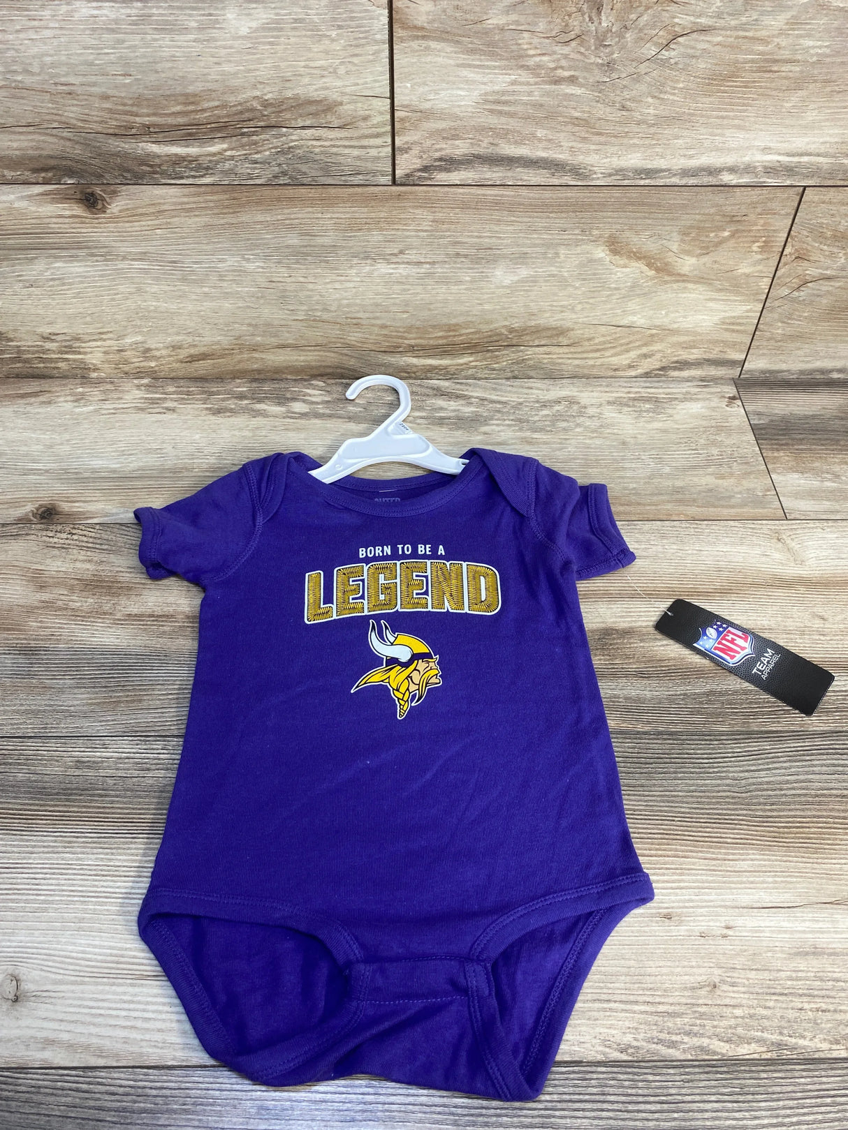 Purple baby onesie with "Born To Be A Legend" text and a yellow Viking helmet logo, NFL tag visible