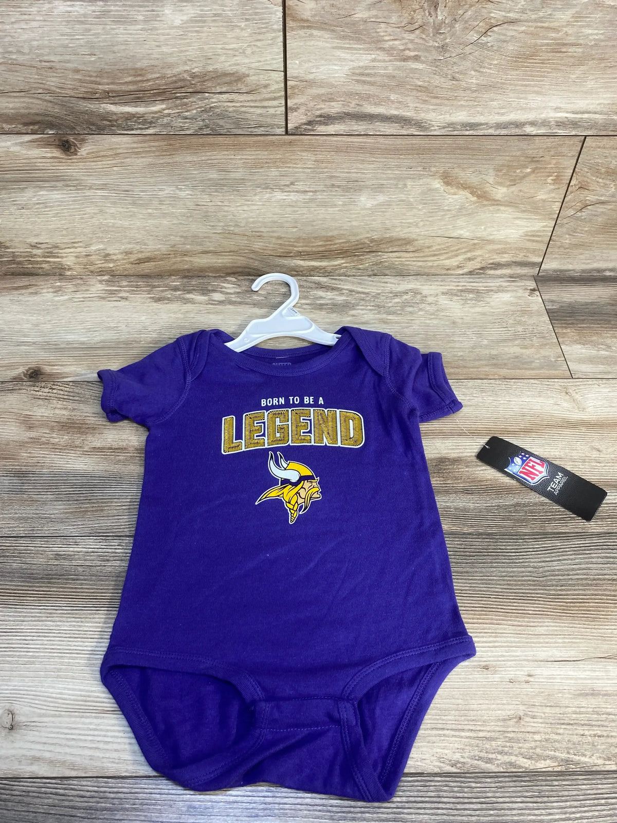 Purple baby onesie with "Born To Be A Legend" text and a yellow Viking helmet logo, NFL tag visible