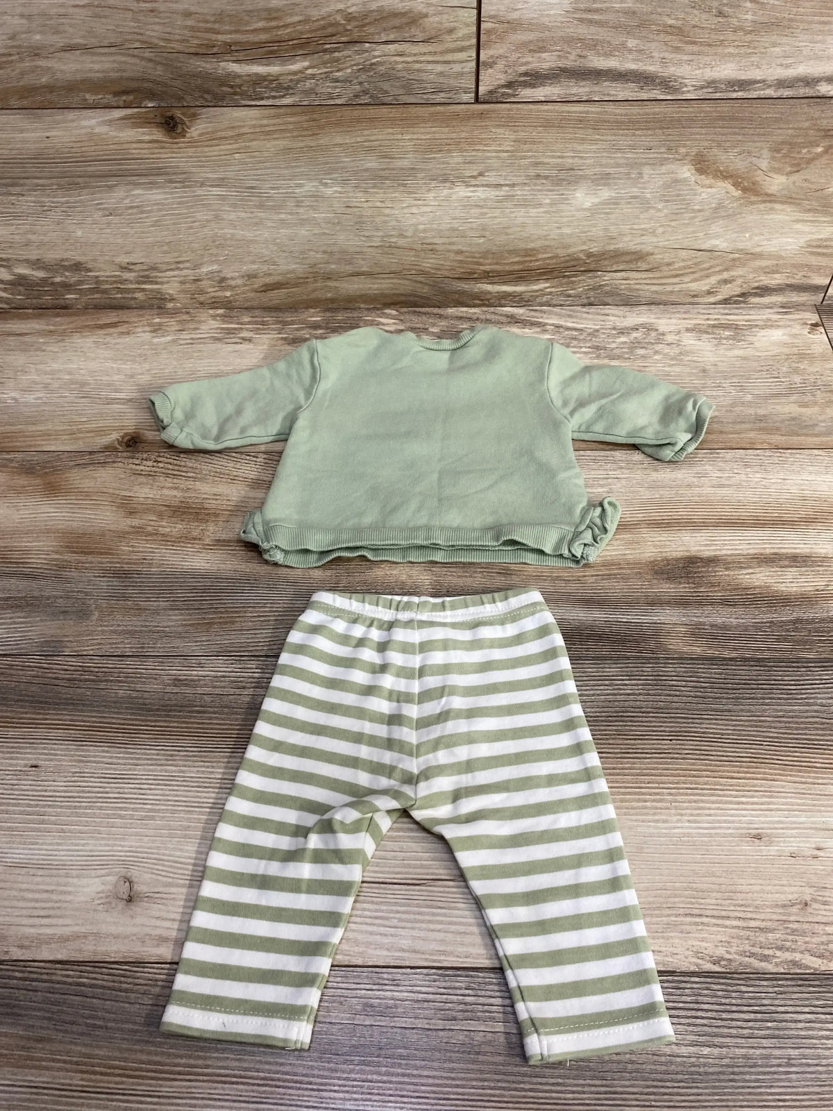 Two-piece baby outfit with sage green long-sleeve top and white leggings with sage green stripes on wood background