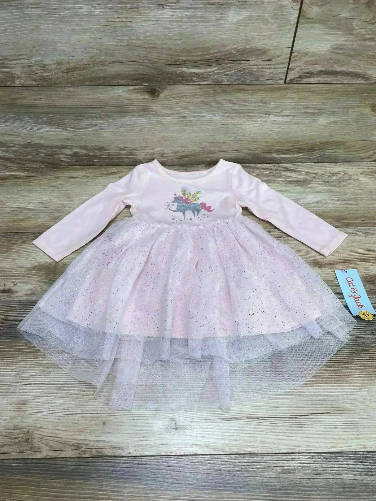 Front view of Cat and Jack pink baby dress with unicorn sequin bodice and layered glitter tulle skirt on wood background