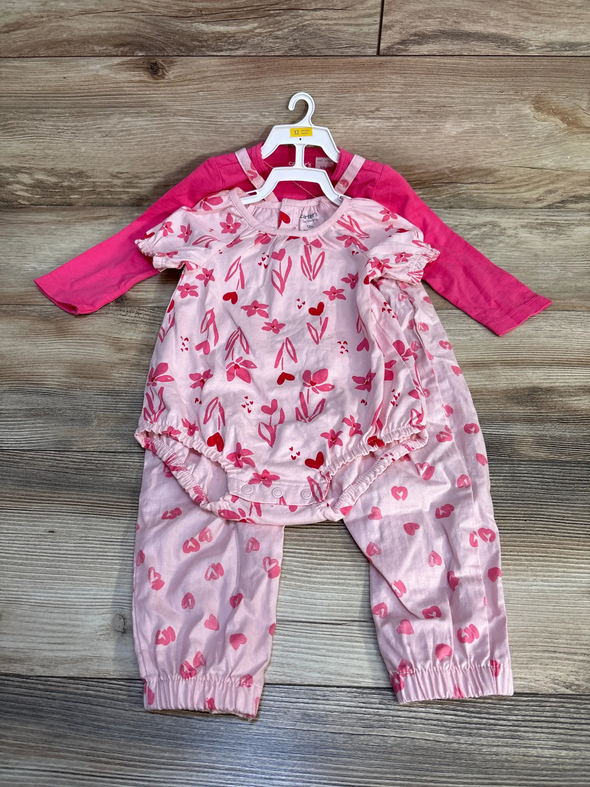 Pink baby girl clothing set with floral and heart patterns on wooden floor