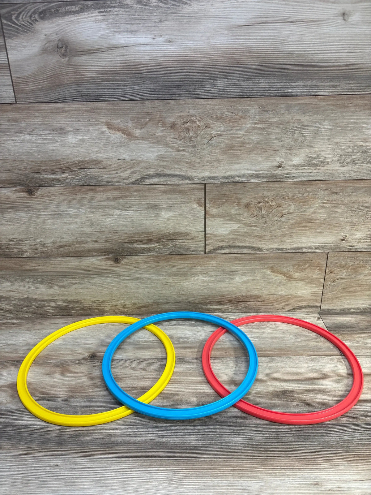 Top-down view of Lovevery Jump-In Hoops and Bean Bags 6pc showcasing three colorful hoops on a wood floor