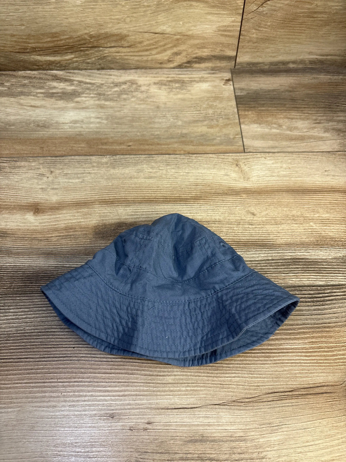 Top view of Carter’s blue bucket hat for ages 0 to 3 months, showcasing its wide stitched brim on a wood-grain floor