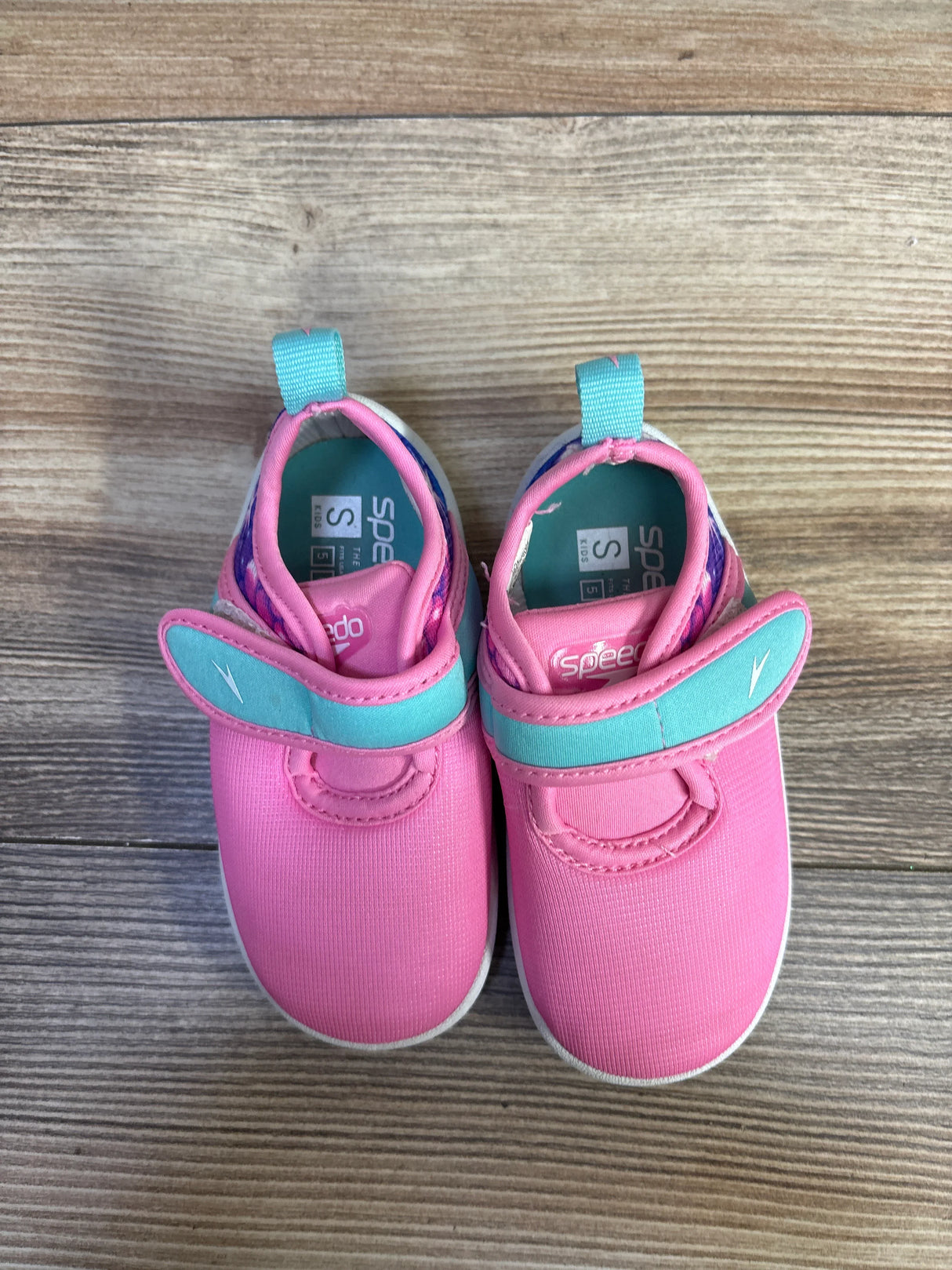 Top view of Speedo Shore Explorer water shoes showcasing pink uppers with teal straps and pull tabs on wood floor