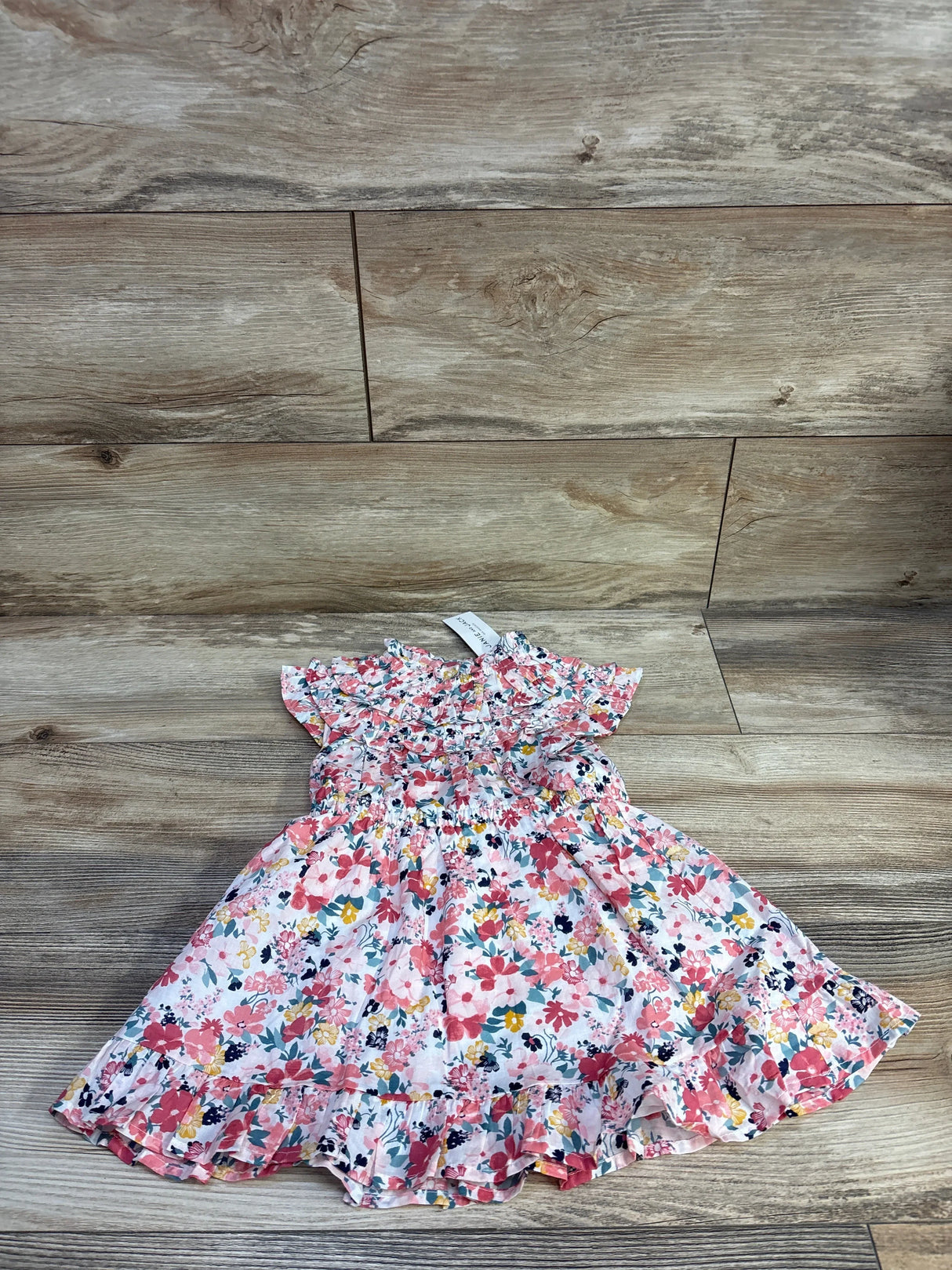 Flat lay of Janie and Jack pink floral toddler dress showcasing ruffle trim and smocked bodice with matching bloomers on wood floor