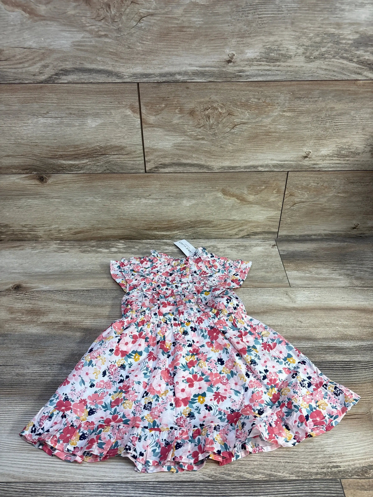 Flat lay of Janie and Jack pink floral toddler dress showcasing ruffled yoke, ruched bodice, and layered hem on wood floor