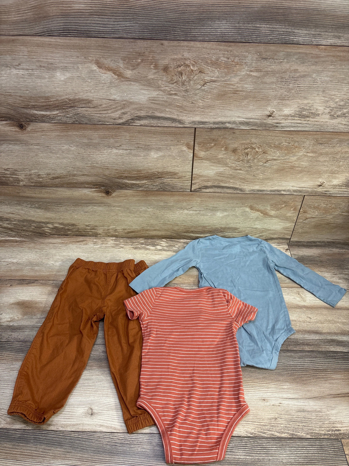 Top-down view of Carter’s 3-piece bodysuit and pant set showing blue and striped bodysuits with brown pants