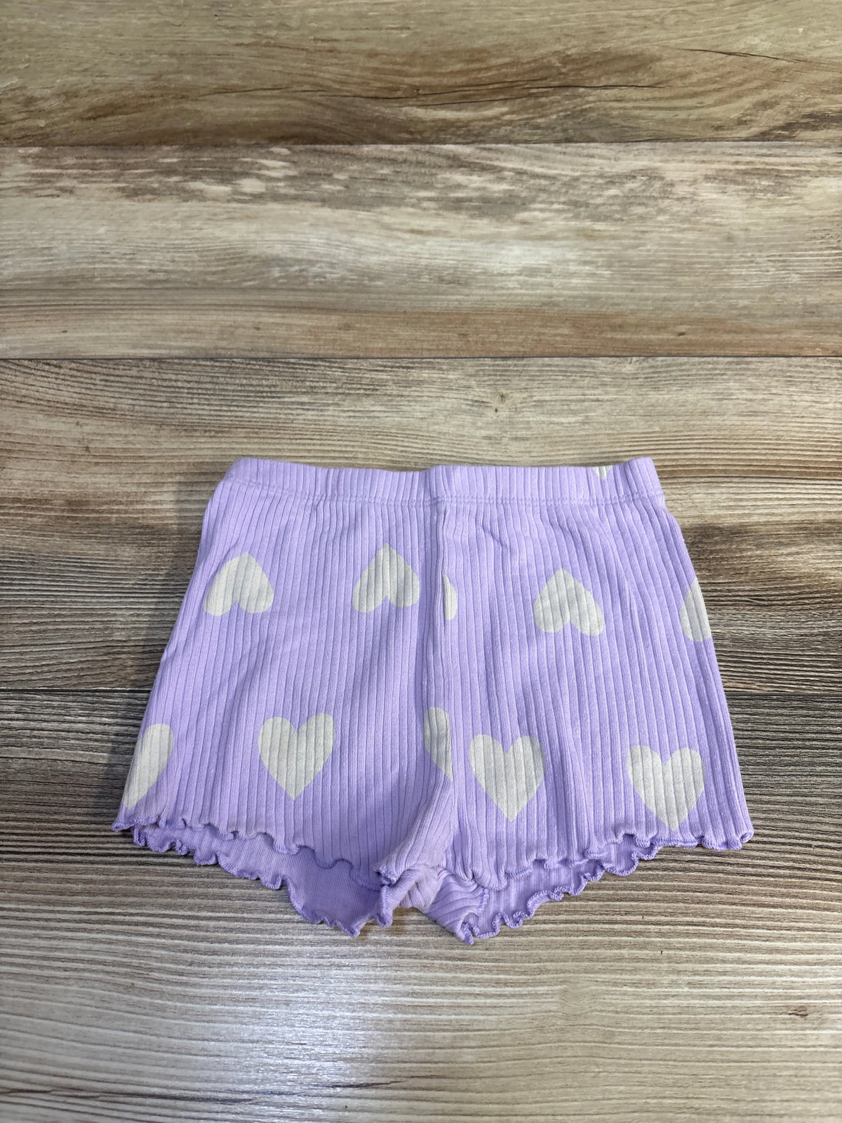 Front view of ribbed toddler bike shorts in lavender with white heart print and lettuce-edge hem on wood background