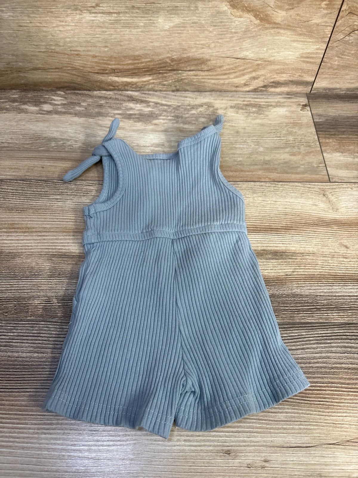 Front view of blue ribbed tank shortie romper showcasing tie shoulder straps on a wood floor