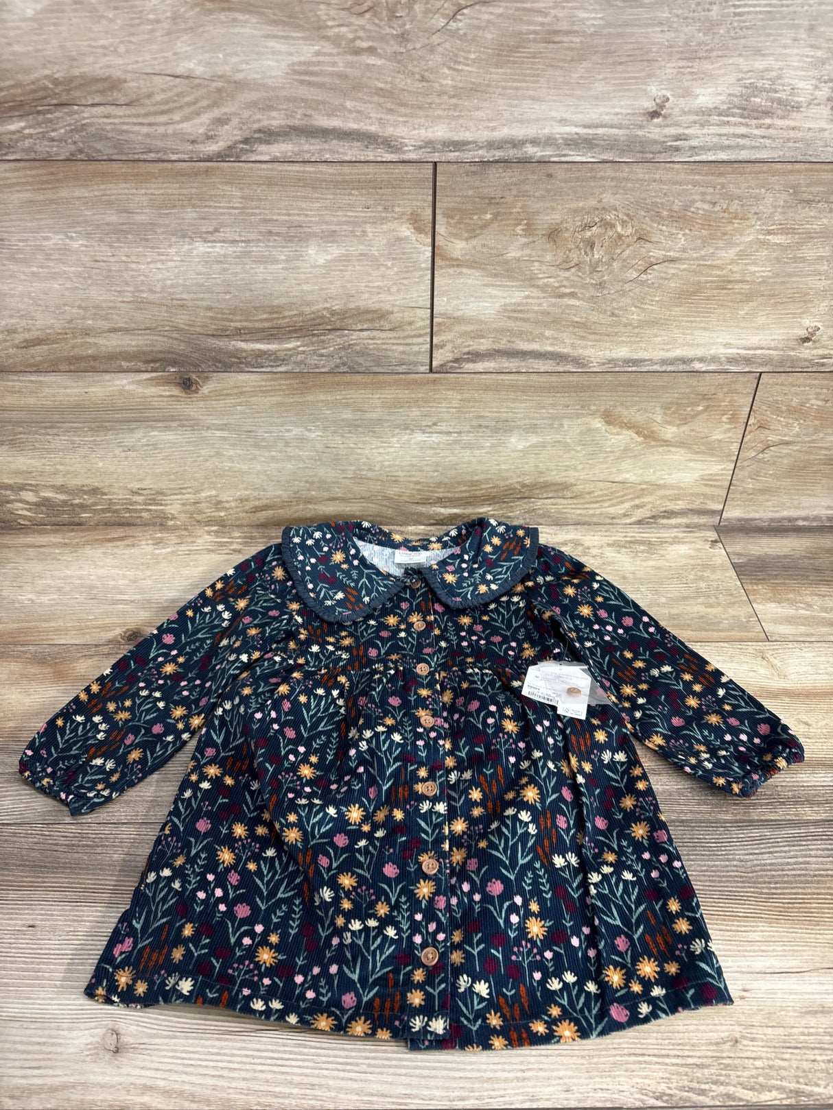 Long sleeve toddler dress with floral print, button front, and Peter Pan collar on wood floor