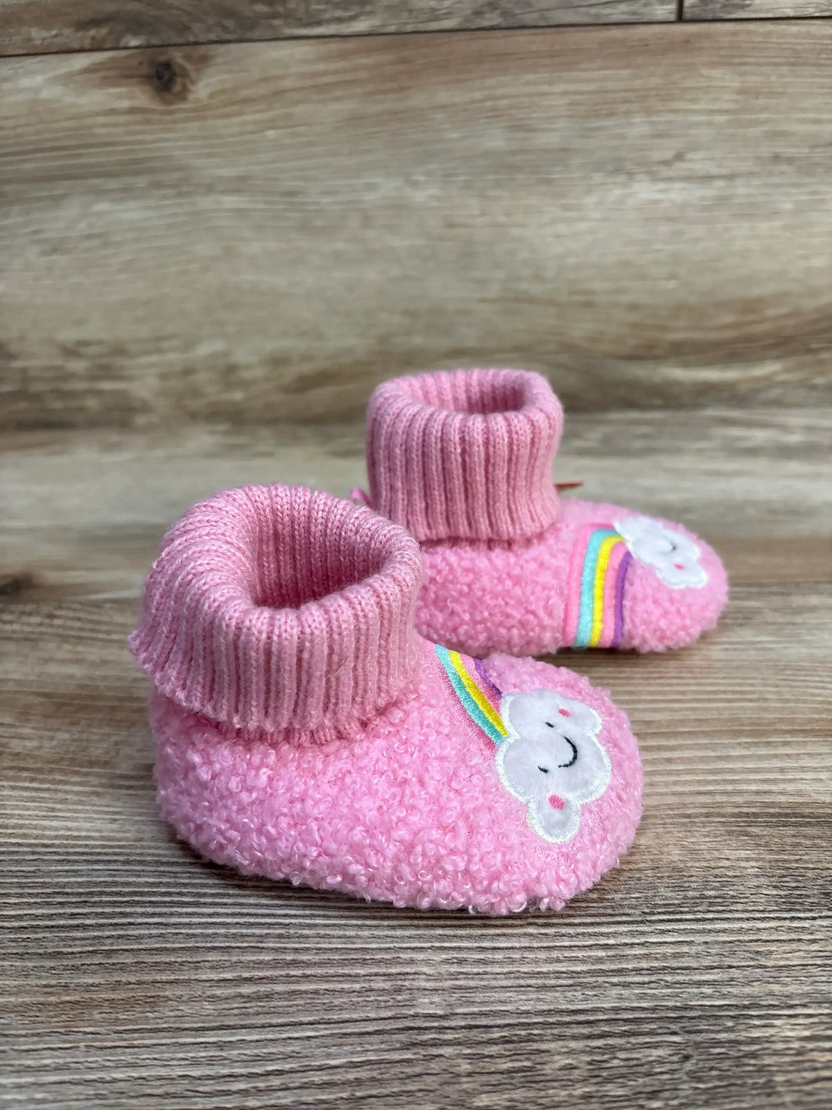 Pink baby booties with smiling cloud and rainbow on wood background