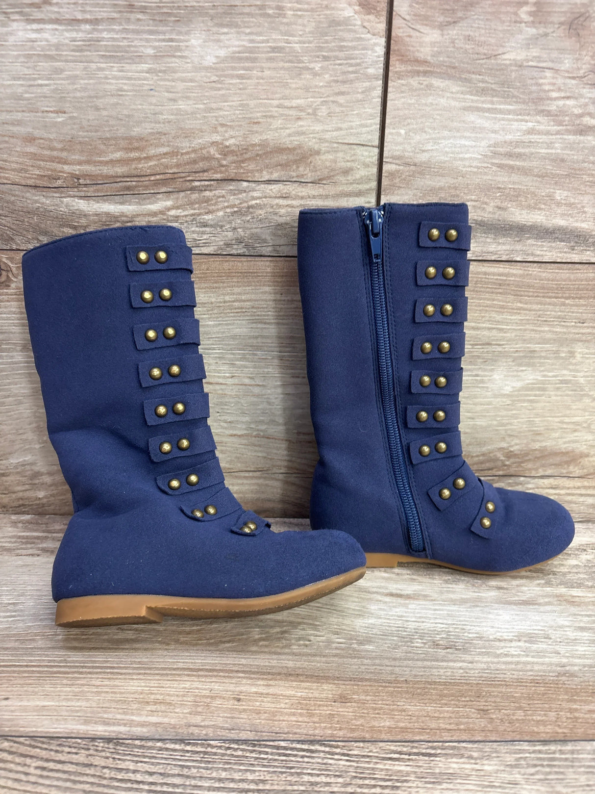 Pair of navy blue toddler boots with gold studs and side zipper on wooden floor background