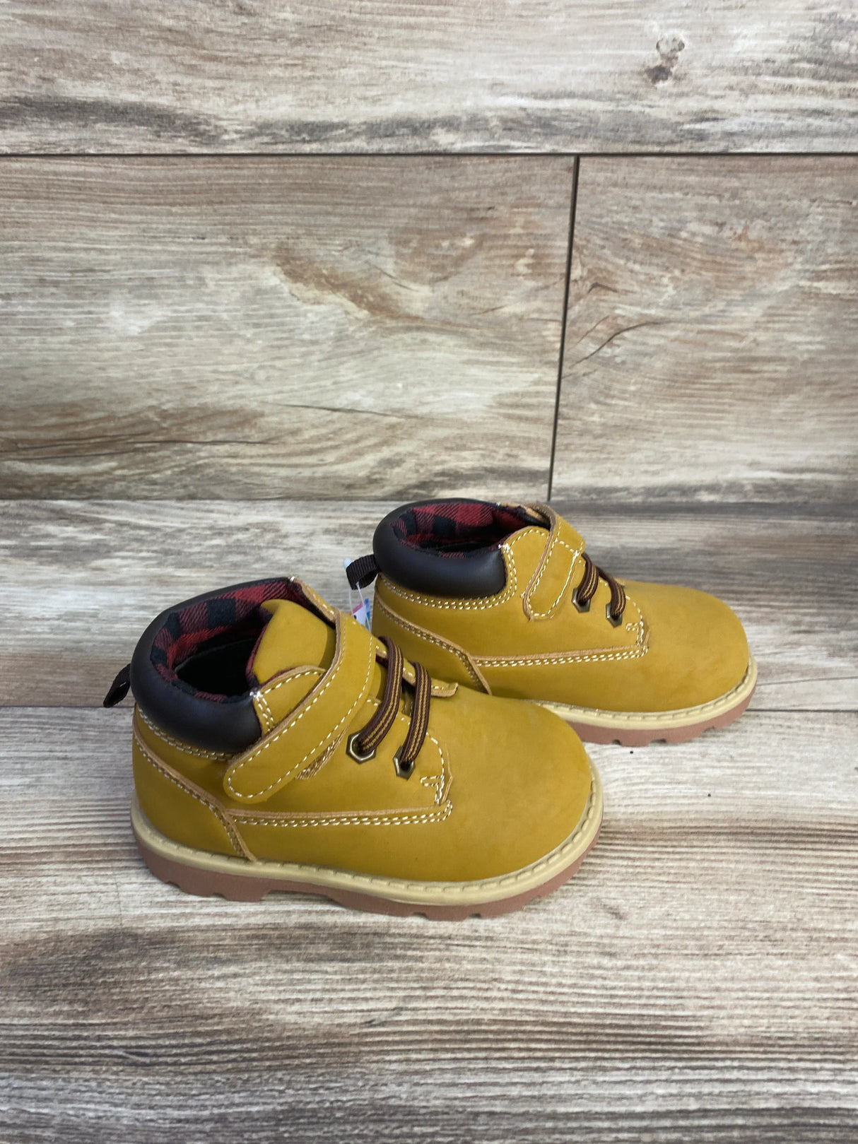 Three-quarter view of toddler Garanimals brown ankle boots with hook-and-loop strap, laces, padded collar, and treaded sole on wood floor