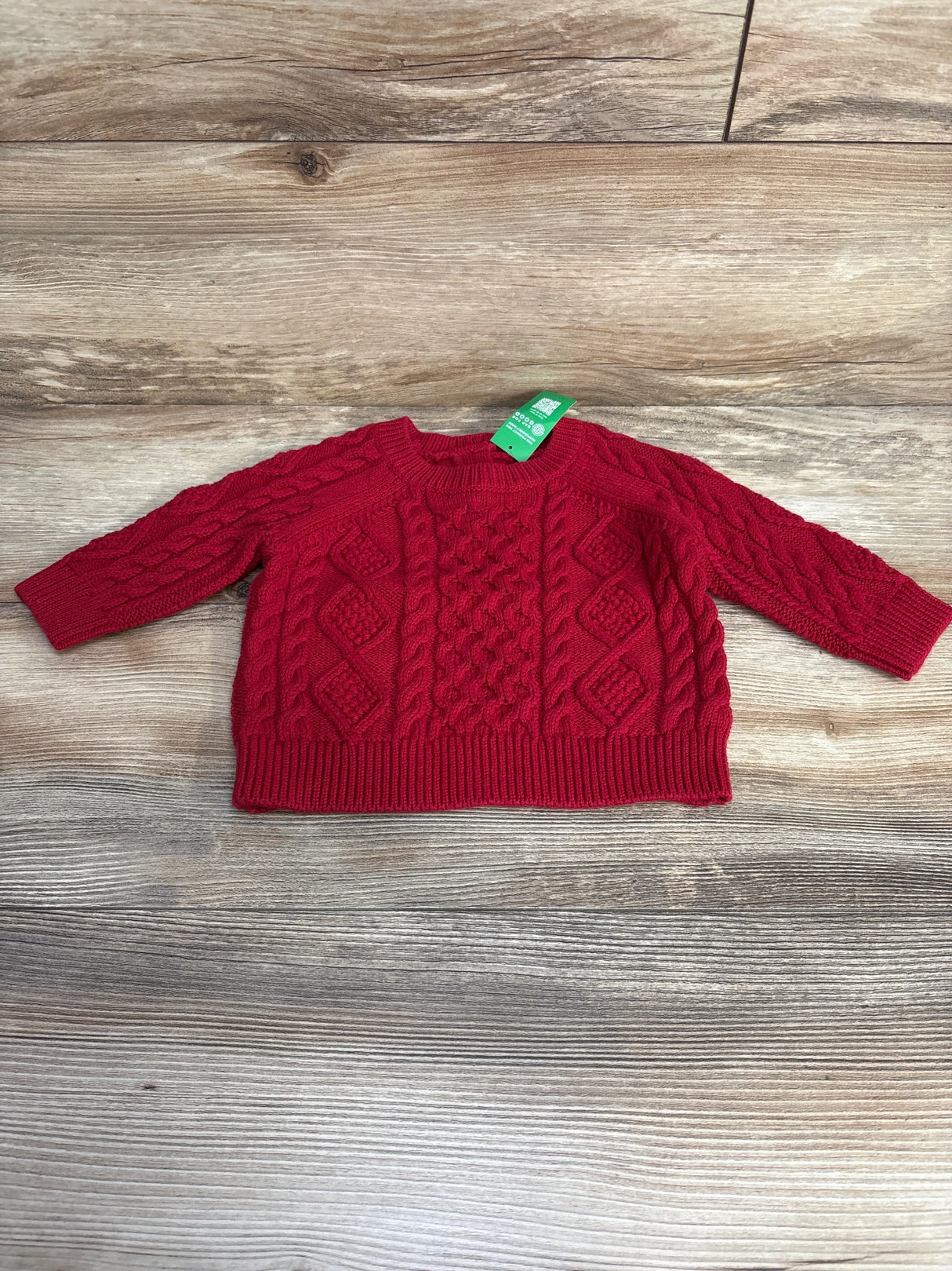 Flat lay of red Baby Gap cable knit sweater, size 3-6m, with crew neck, braided cable pattern and ribbed hem on wood background