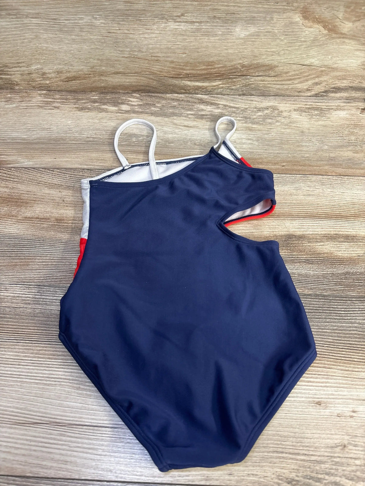 Side view of Red White Blue 1pc Cut-Out Swimsuit size 5T in navy with red and white side panels and waist cutout on wood plank floor