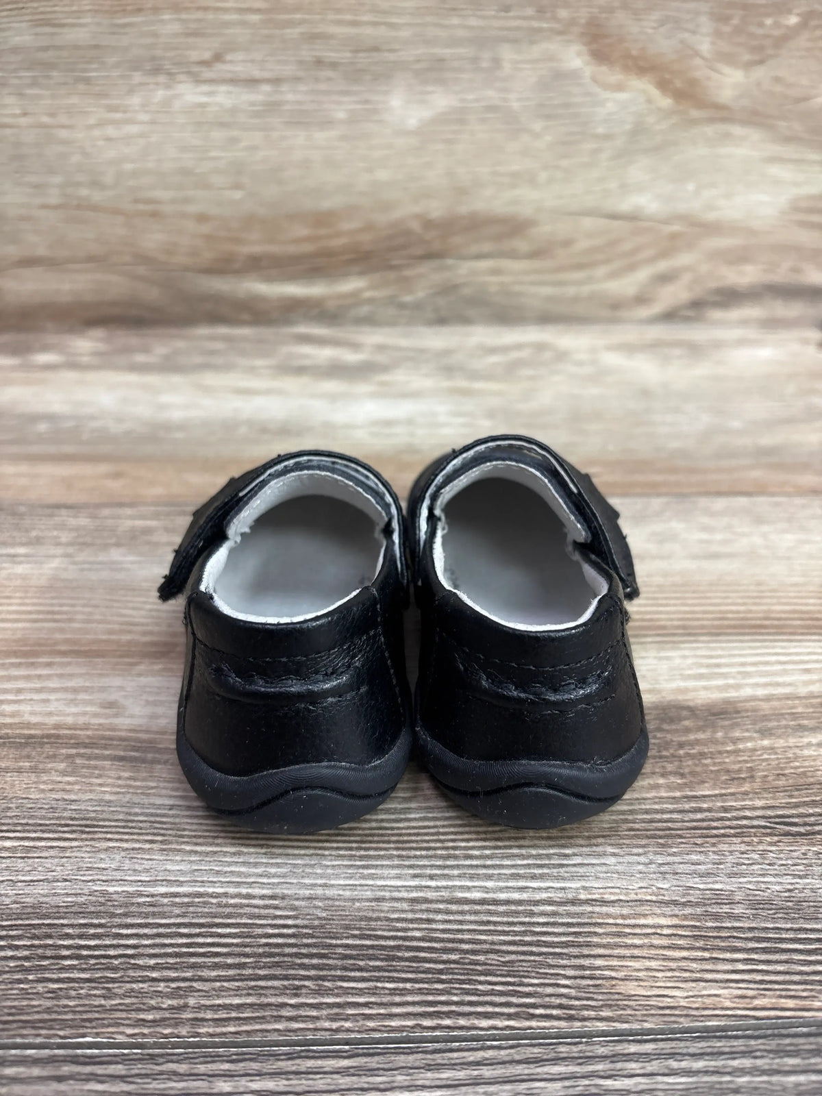 Rear view of Pediped Grip n’ Go Charlie loafers showcasing black uppers and hook-and-loop straps with a wood-grain background