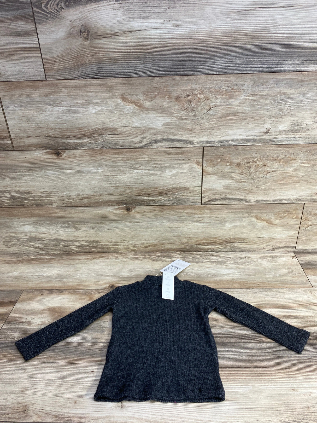 Dark gray long-sleeve ribbed toddler sweater laid flat on wooden floor with tag attached