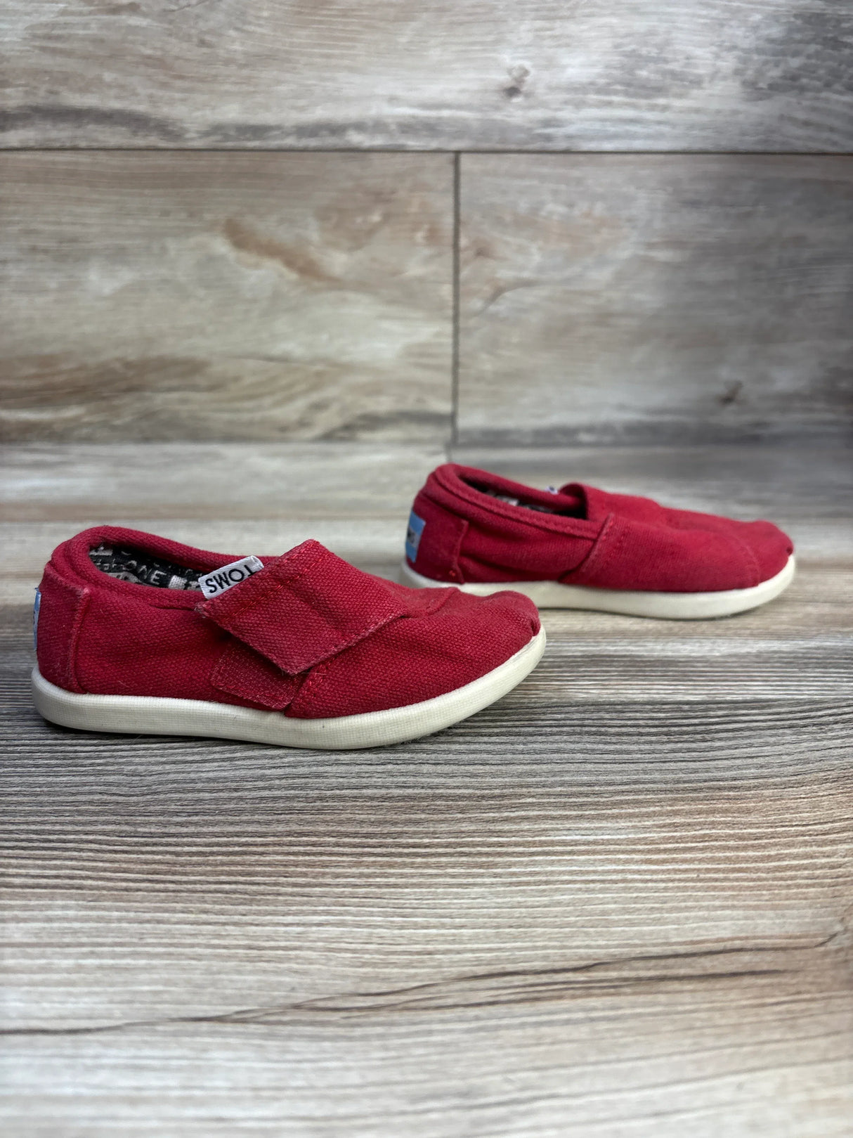 Pair of red TOMS slip-on toddler shoes with white soles on wood floor