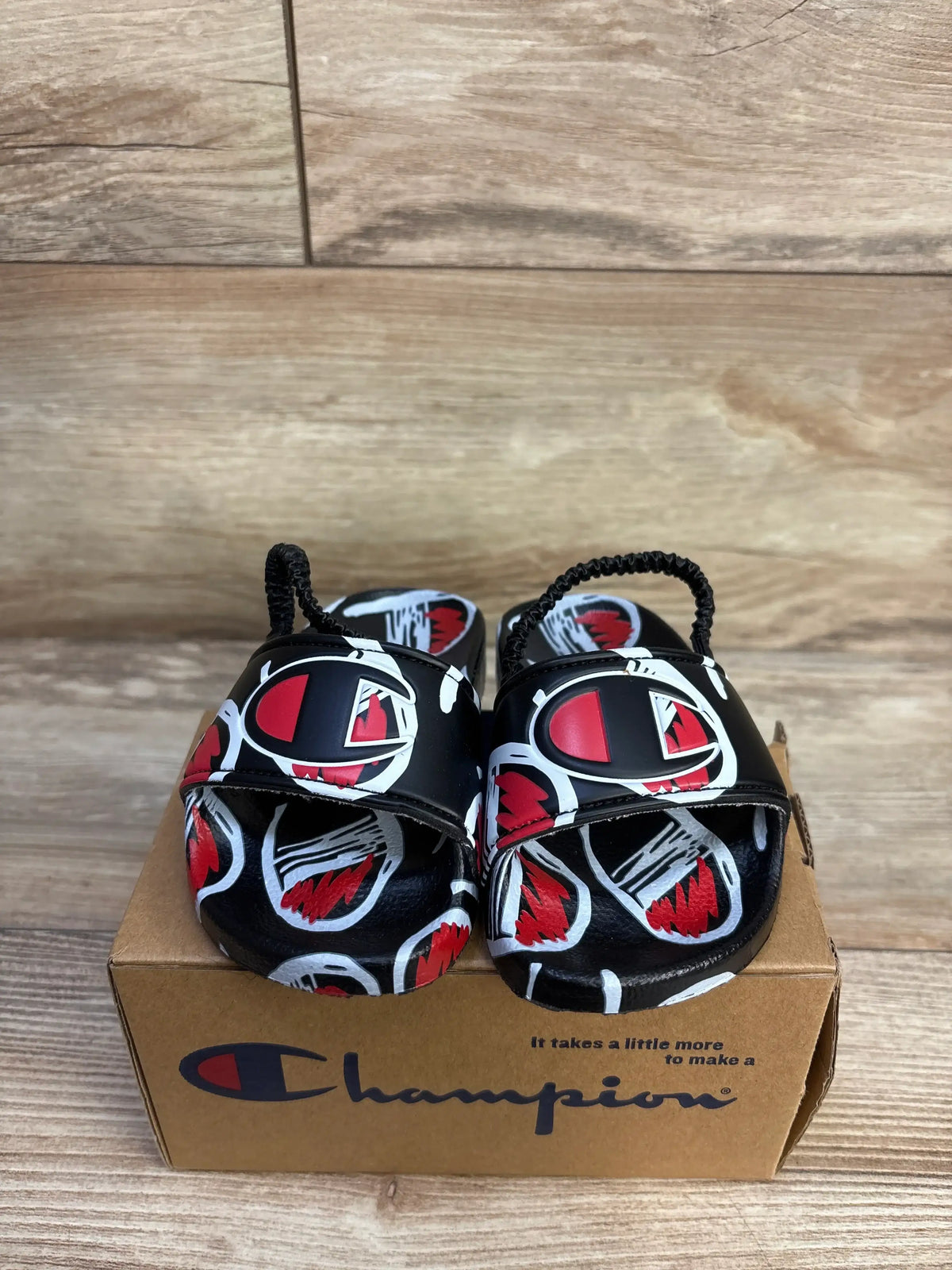 New Me n Mommy To Be black comic print slide sandals on a brown branded box.