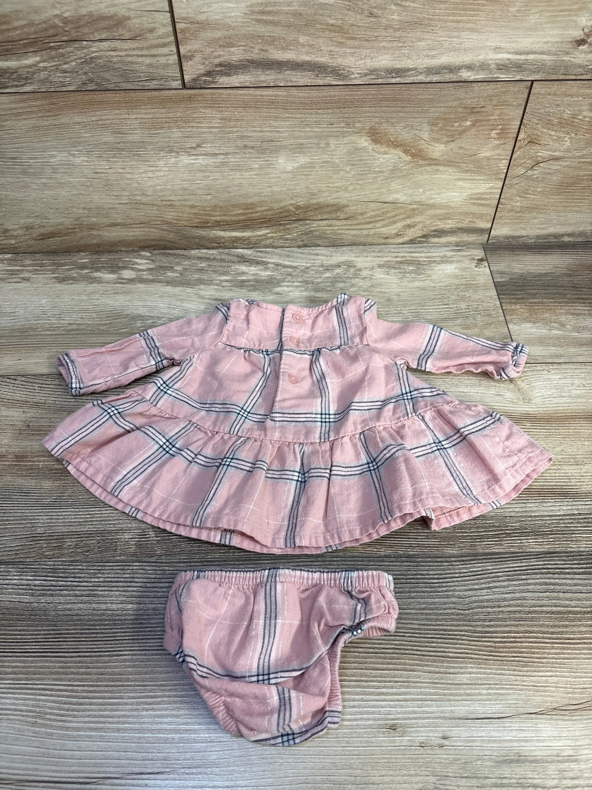Top view of Carter’s pink long sleeve dress and bloomers set showcasing plaid pattern with wood floor background
