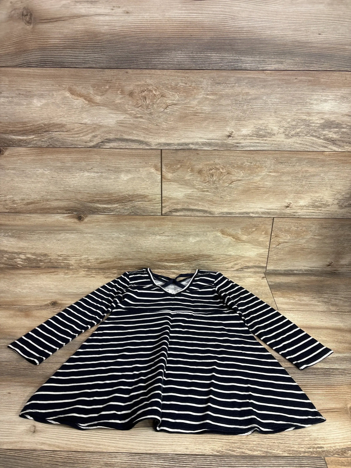 Flat lay of Baby Gap girls navy and white striped cross-back long-sleeve dress size 5T showcasing A-line swing skirt on wood background
