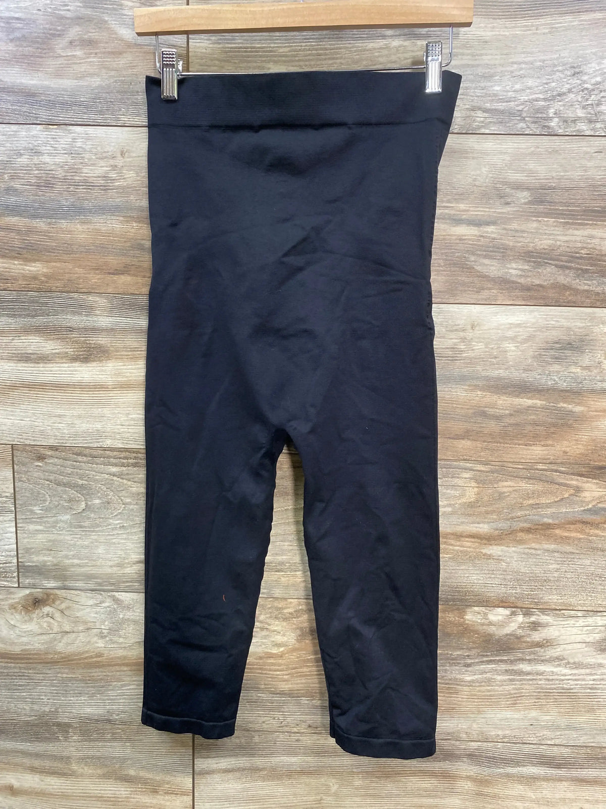 Black high-waisted leggings hanging on wood background, cropped length pants