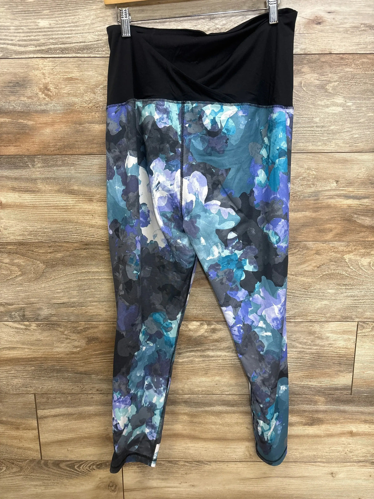 Front view of Isabel maternity leggings in blue watercolor print with black fold-over belly panel on wooden background