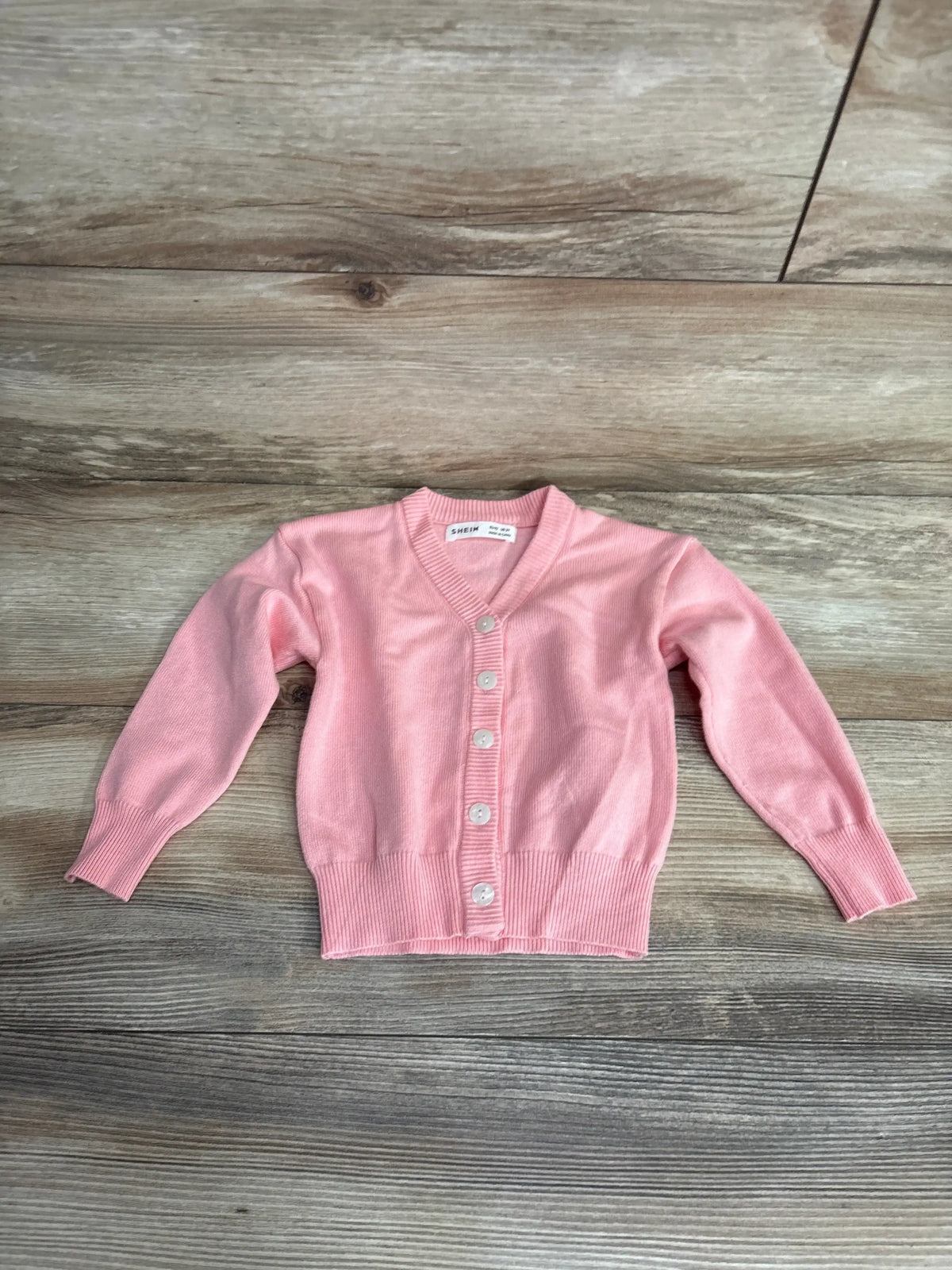 Pink button-up kids cardigan sweater on wooden background